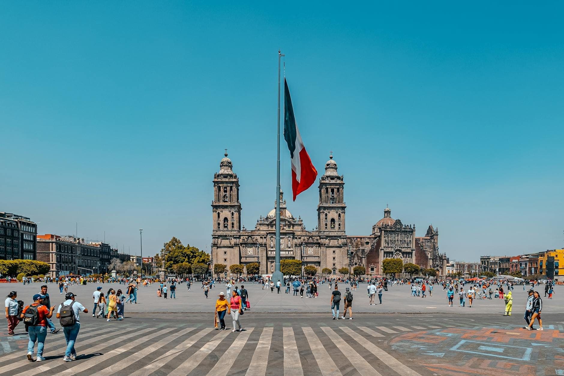 Wide view of Mexico City’s Zócalo square with the Metropolitan Cathedral, giant flag, and people walking on a sunny day.