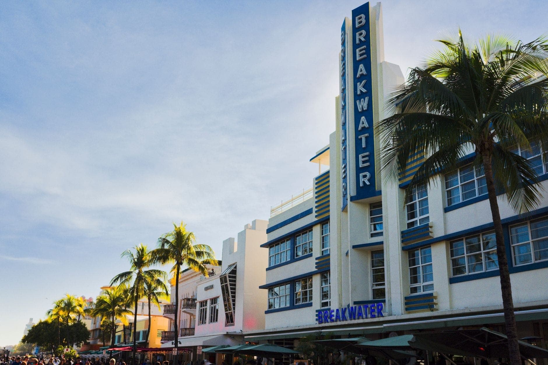Colorful Art Deco buildings with palm trees and sidewalk cafes on a sunny day in Miami's historic Ocean Drive district.