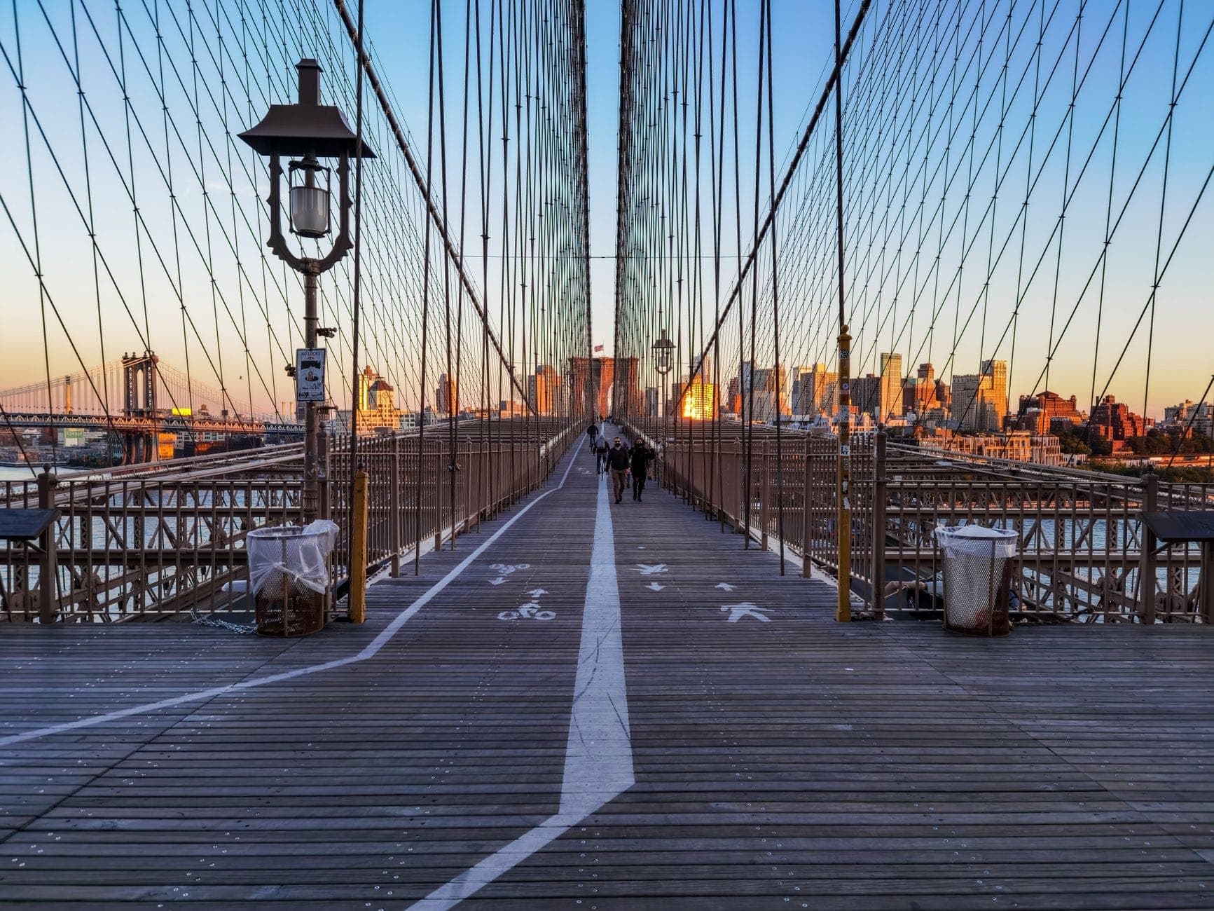 นักท่องเที่ยวเดินบน Brooklyn Bridge พร้อมวิวสกายไลน์ของ Manhattan ยามพระอาทิตย์ตก ประสบการณ์คลาสสิกฟรีใน New York City