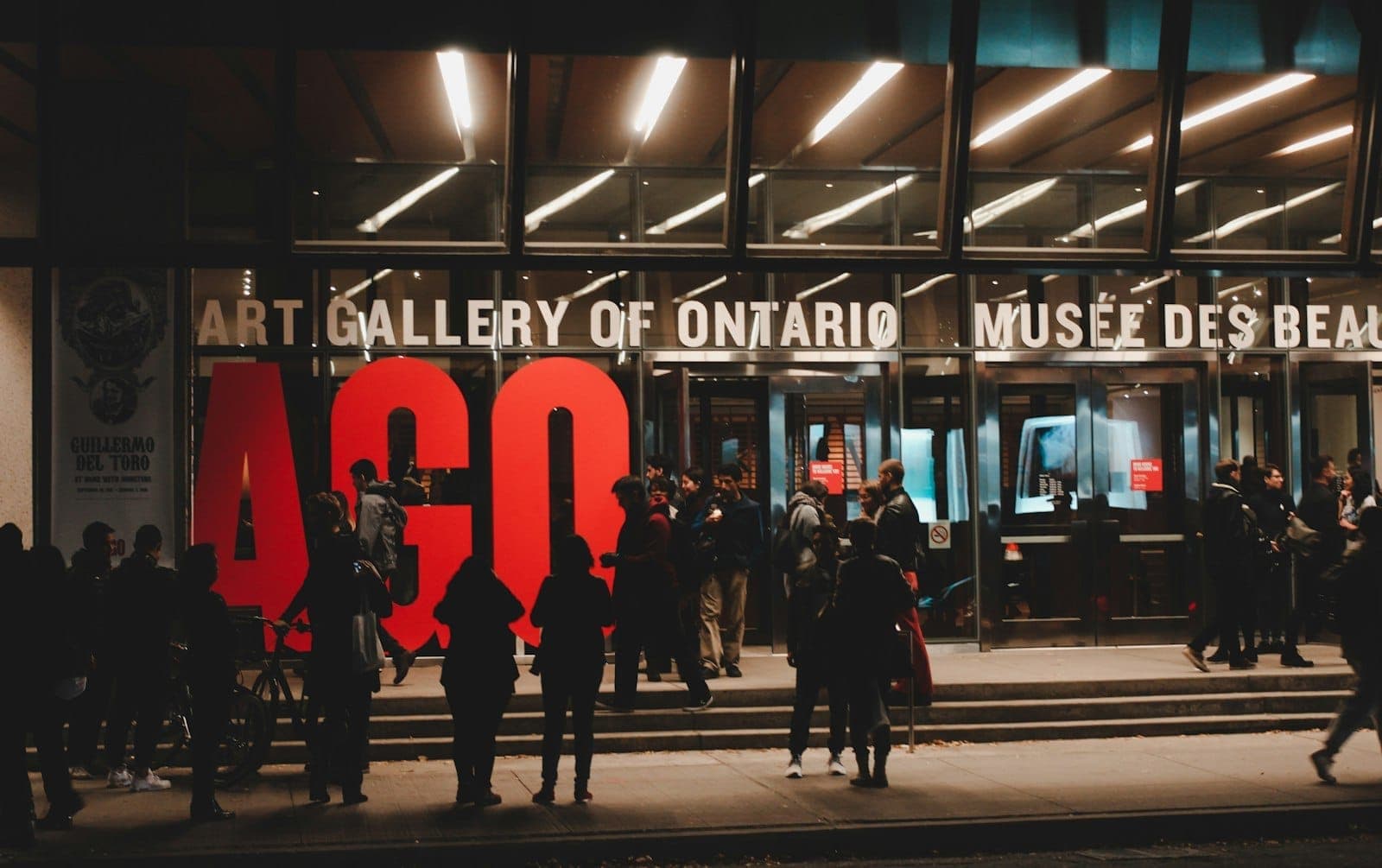 Folla riunita davanti all'ingresso dell'Art Gallery of Ontario di notte, con le grandi lettere AGO visibili sopra le porte.