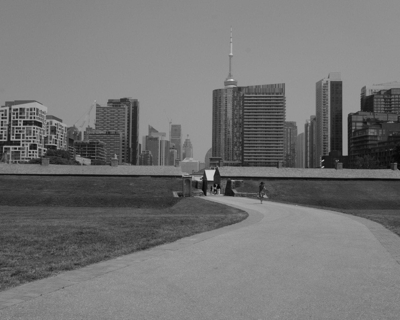 Vista di Fort York con lo skyline di Toronto e la CN Tower sullo sfondo, sentiero che conduce alle storiche mura del forte, in bianco e nero.