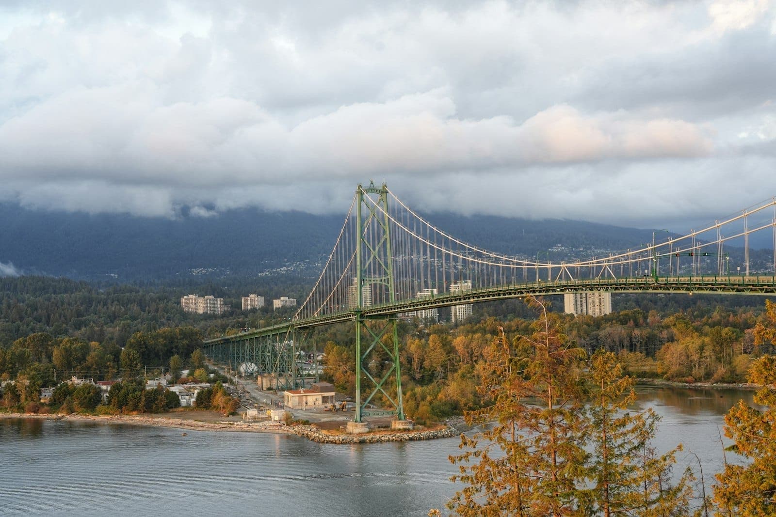 Lions Gate Bridge ในแวนคูเวอร์มองจากด้านบนพร้อมต้นไม้ในฤดูใบไม้ร่วงและภูเขาเป็นฉากหลัง