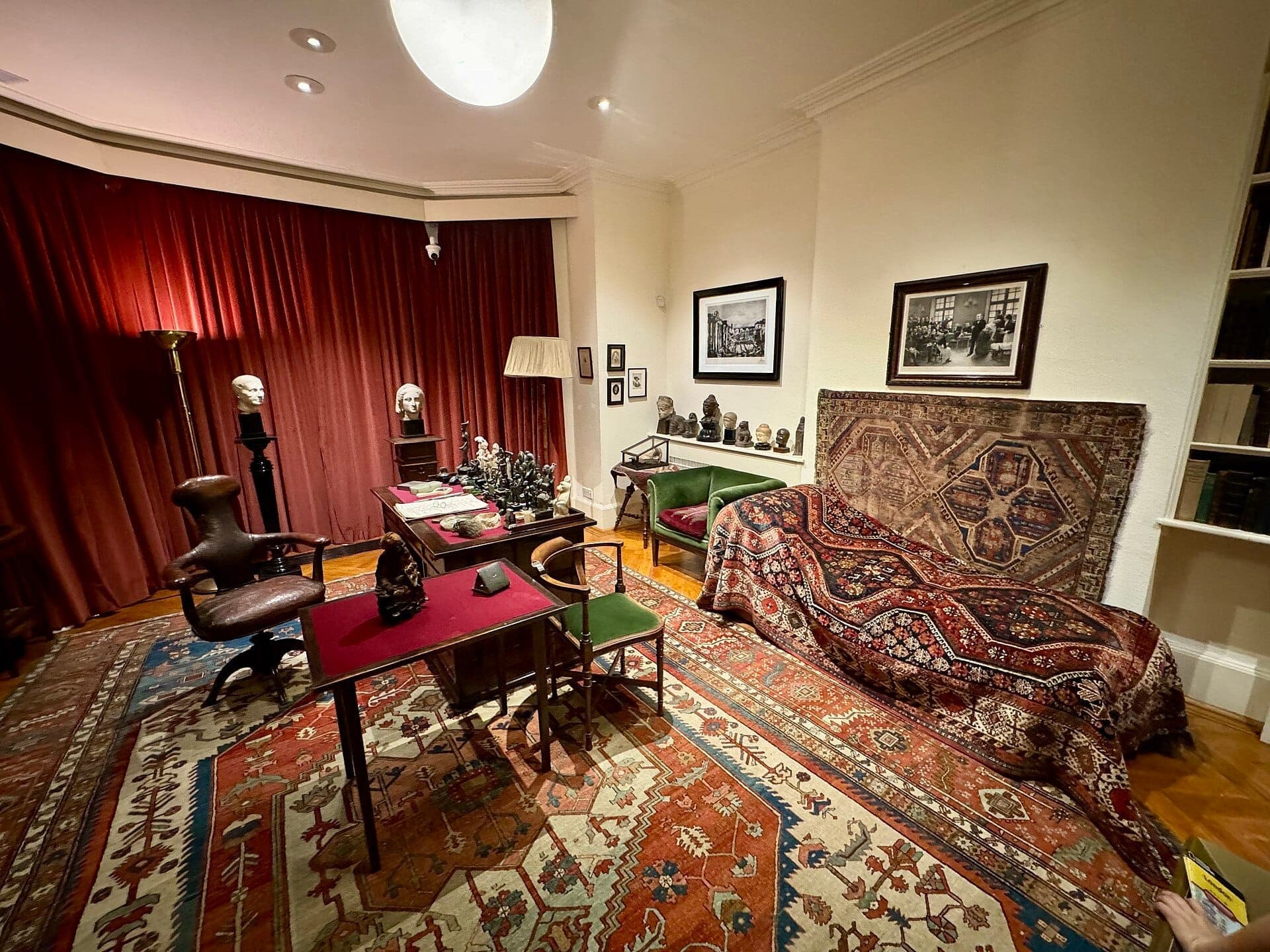 Gabinet w Freud Museum London z kultową kozetką Freuda, ozdobnymi dywanami, antycznym biurkiem i ścianami pełnymi dzieł sztuki w ciepłym oświetleniu.
