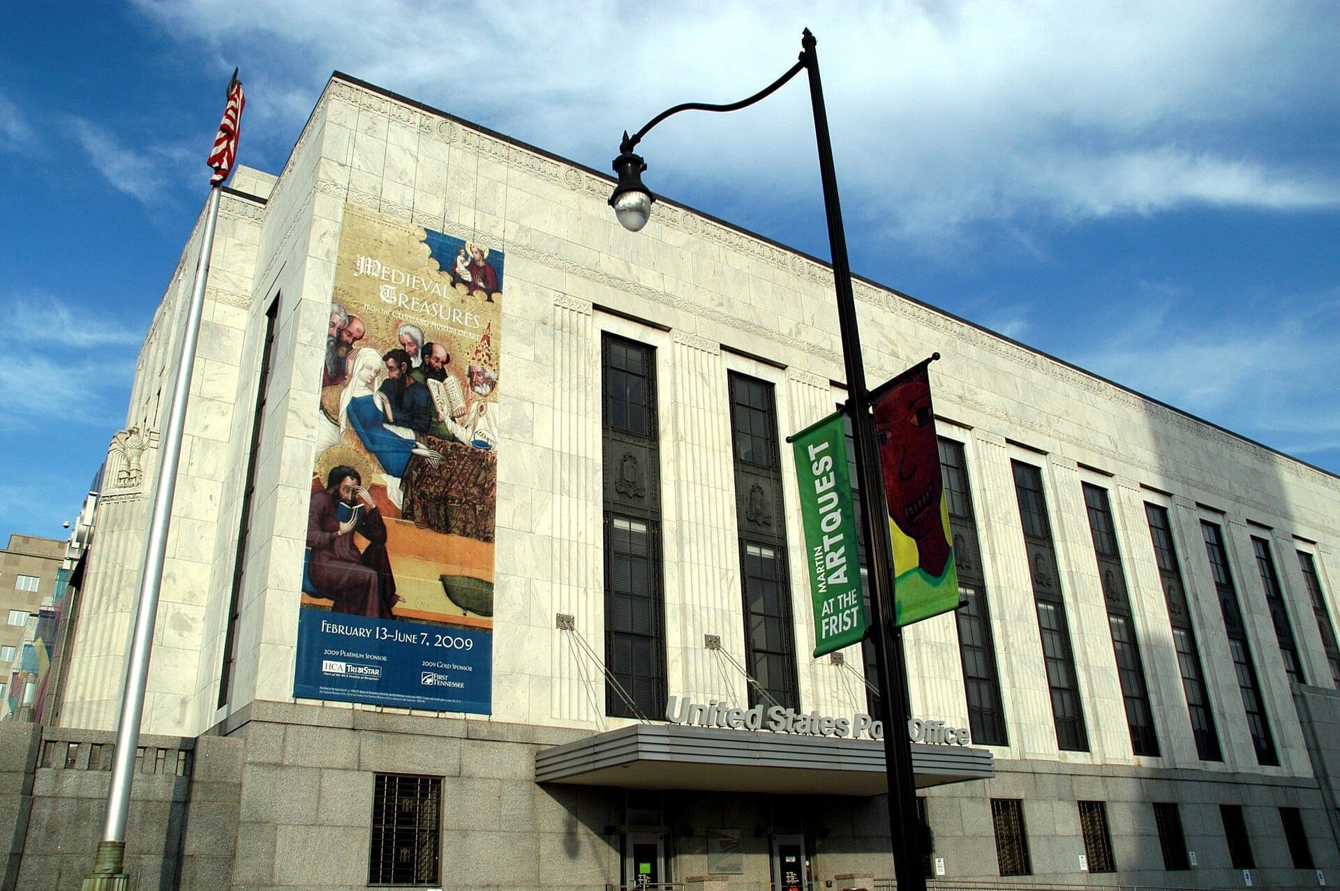 Exterior view of the Frist Art Museum in Nashville, showcasing its grand Art Deco architecture and large windows under a blue sky.