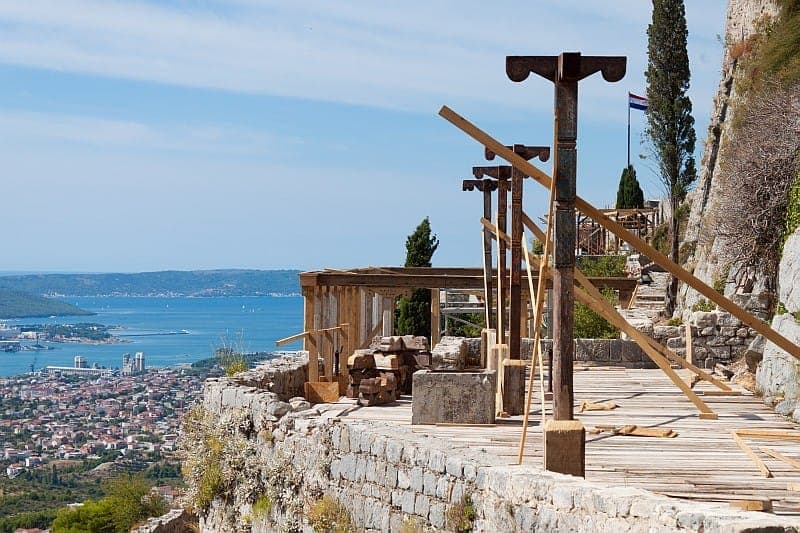 Strutture in legno del set cinematografico lungo le mura della Fortezza di Klis, con vista sulla città di Split e la costa adriatica sotto un cielo azzurro limpido.