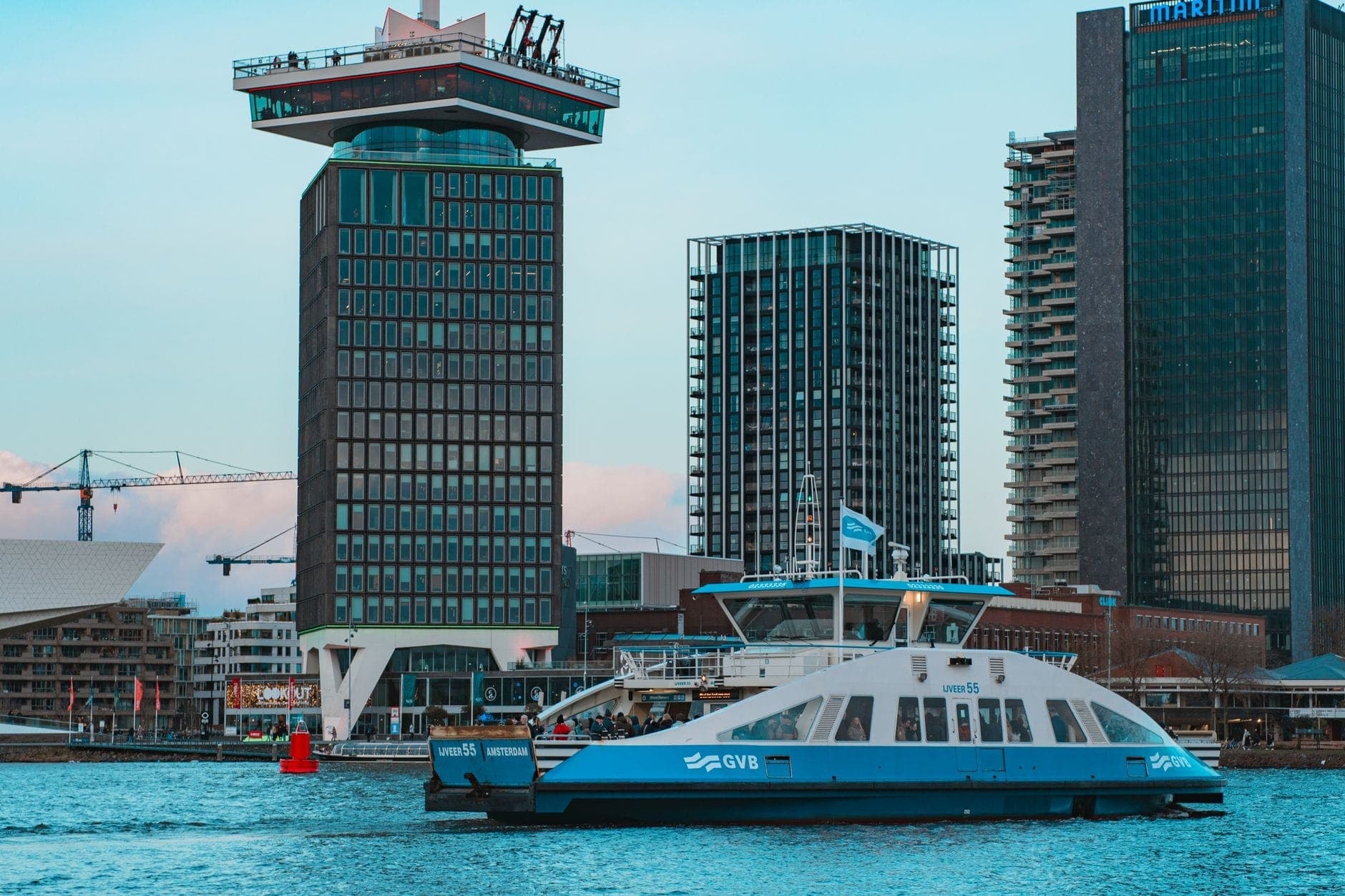 GVB-Fähre überquert den Fluss IJ in Amsterdam mit dem A'DAM Tower und modernen Gebäuden im Hintergrund.