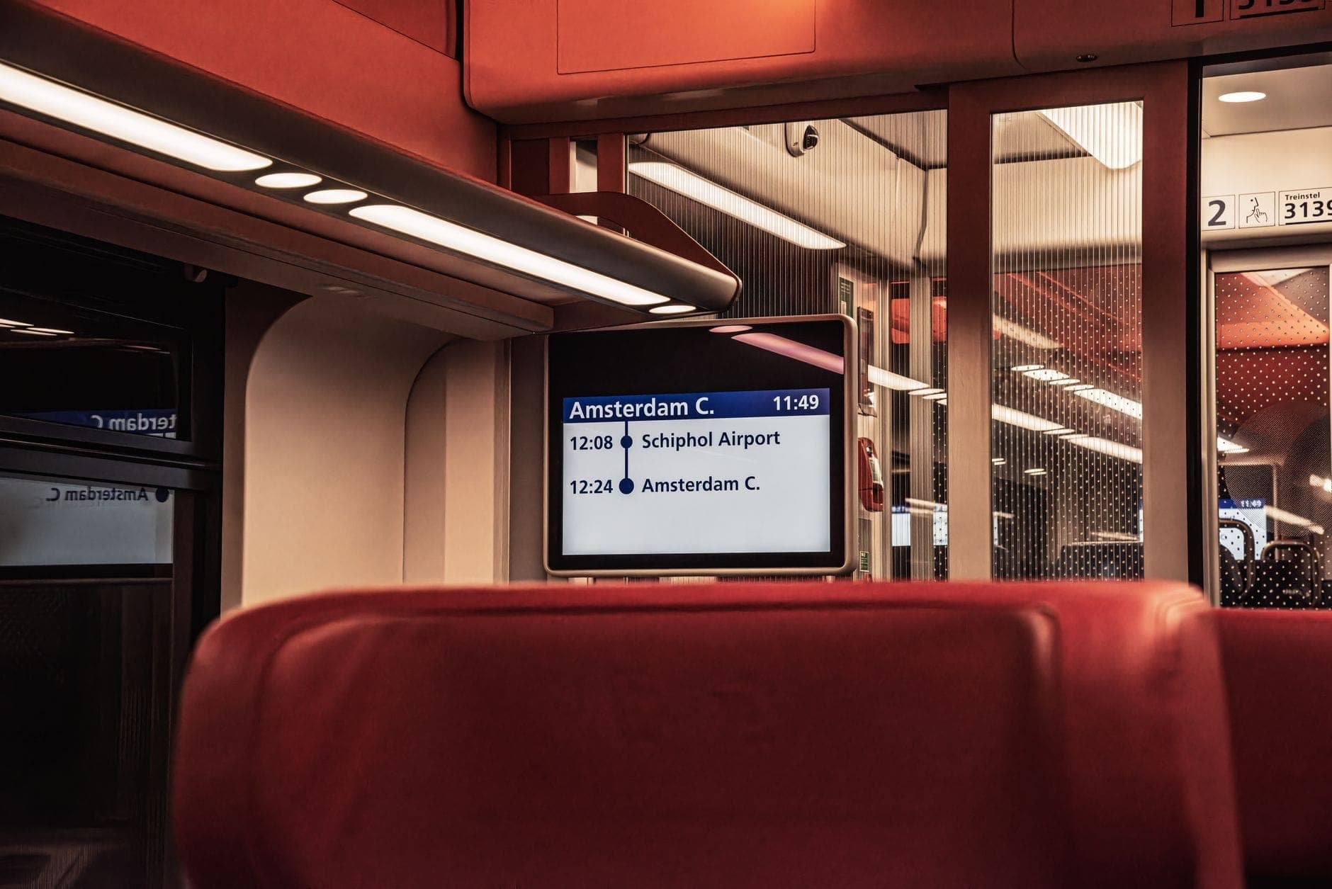 Inneres eines Zuges mit einem digitalen Bildschirm, der die Route vom Flughafen Schiphol zum Amsterdamer Hauptbahnhof anzeigt.