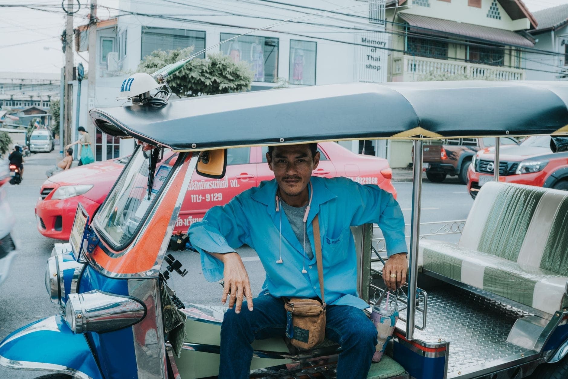Chiang Mai sokaklarında mavi tuk-tuk'unda oturan bir tuk-tuk sürücüsü, arka planda kentsel binalar ve trafik.