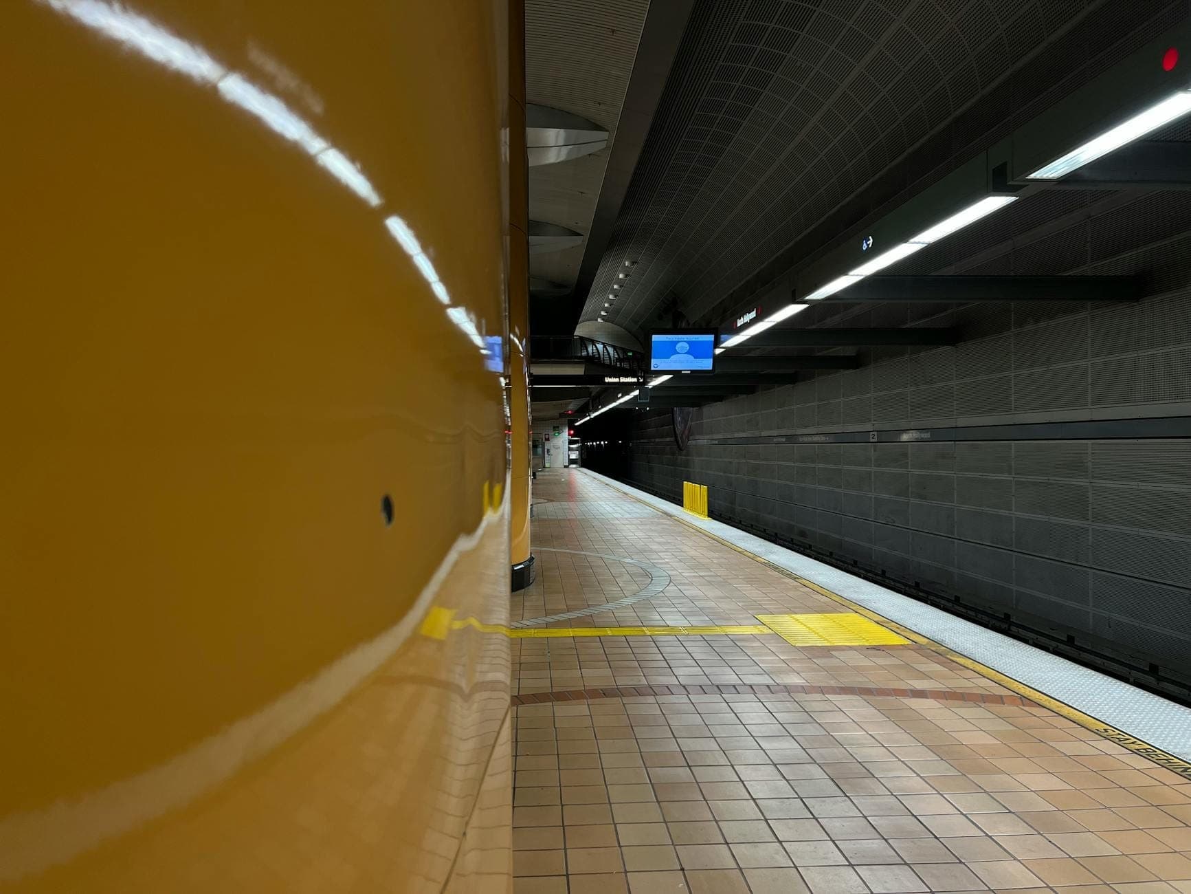 Wide view of a clean CTA 'L' train platform with yellow columns and signs, suggesting a Chicago transit station, possibly the Orange Line.