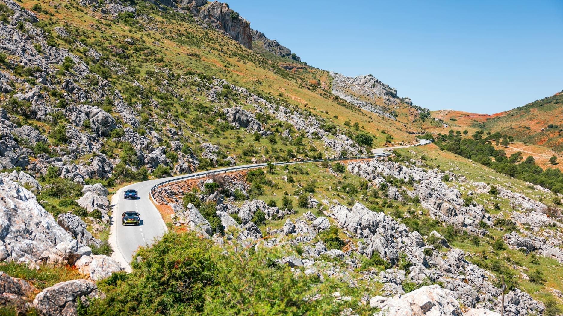 Kurvenreiche Bergstraße mit Autos auf felsigem Gelände unter klarem blauem Himmel, typisch für ländliche Straßenverhältnisse auf Kreta.