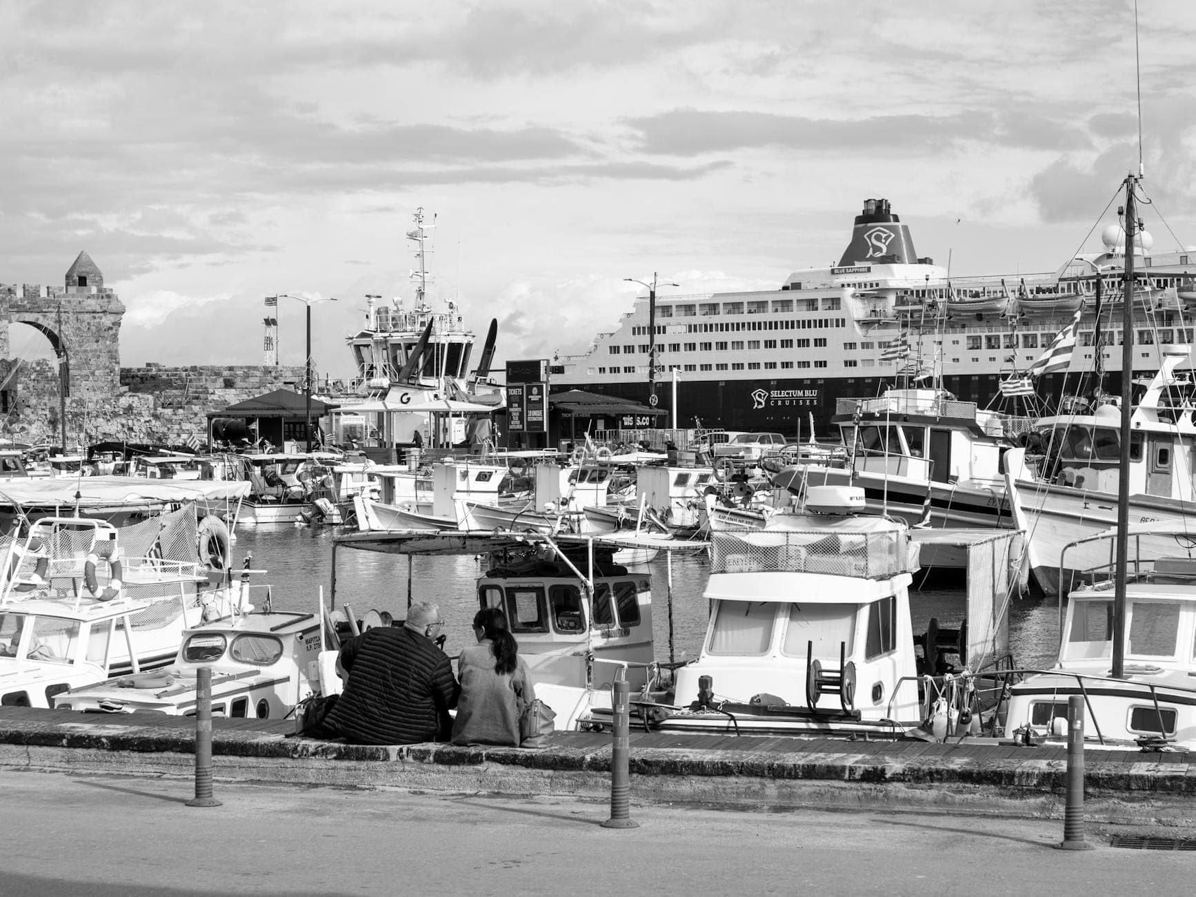 Hafen von Heraklion auf Kreta mit festgemachten Fähren, Fischerbooten und Menschen, die am Ufer sitzen, zur Veranschaulichung der Fährverbindungen.