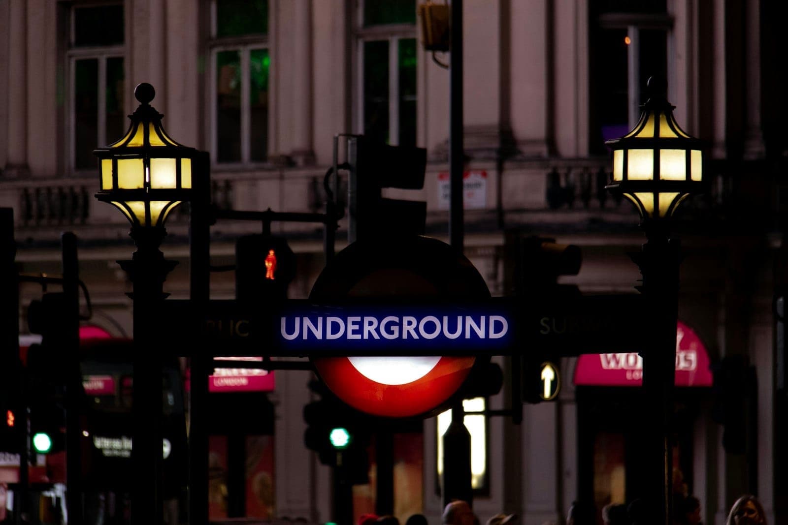 Знаменитая вывеска входа в London Underground с горящими фонарями ночью на фоне фасада исторического городского здания.
