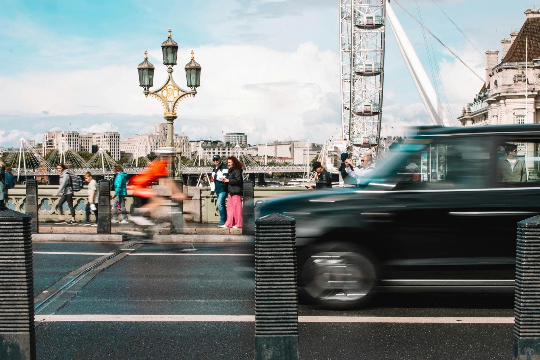 Уличная сцена Лондона с чёрным кэбом, велосипедистом в движении и London Eye на заднем плане на оживлённом мосту.