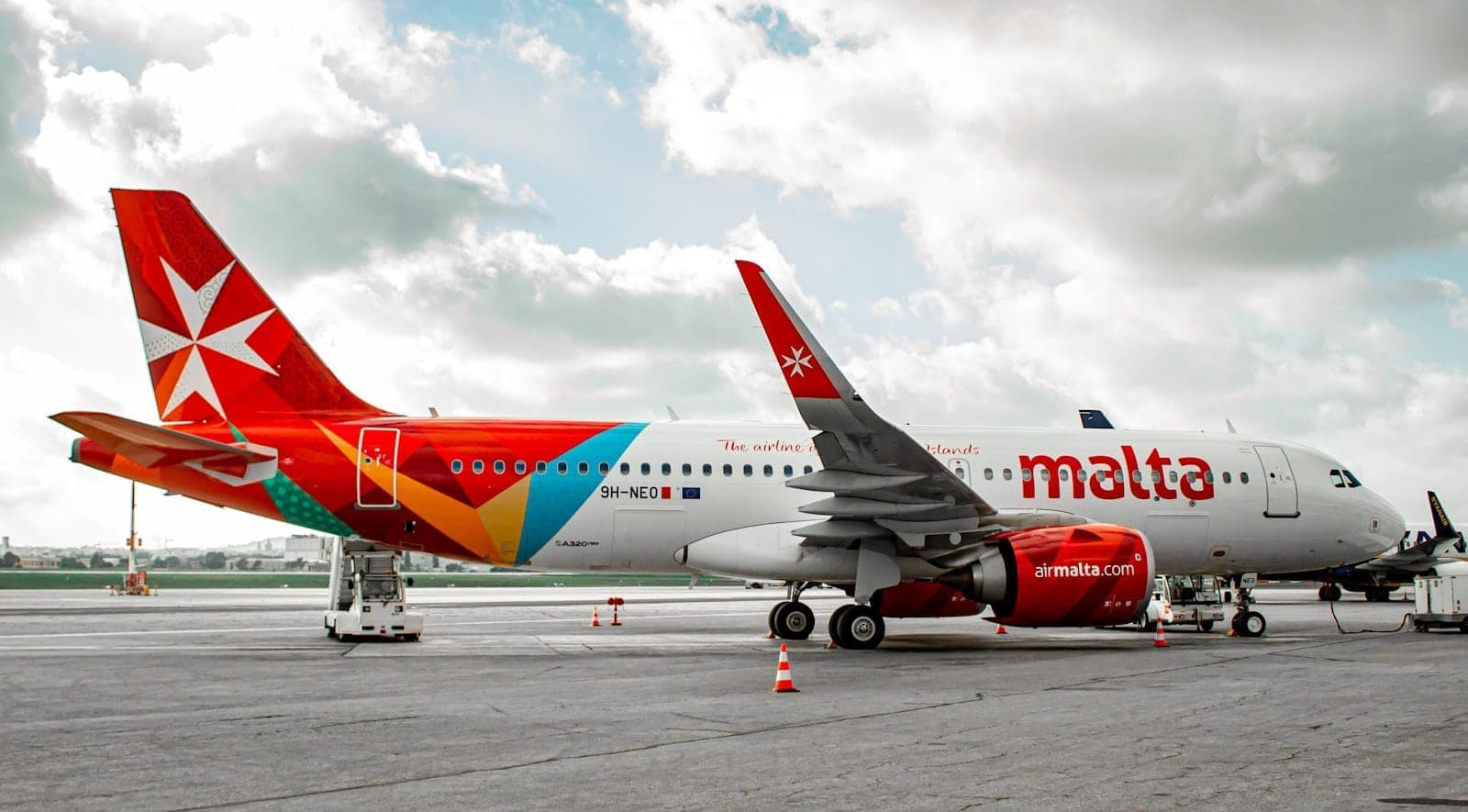 Avión de Air Malta estacionado en la pista del Aeropuerto Internacional de Malta con carros de equipaje y vista clara de la marca de la aeronave.