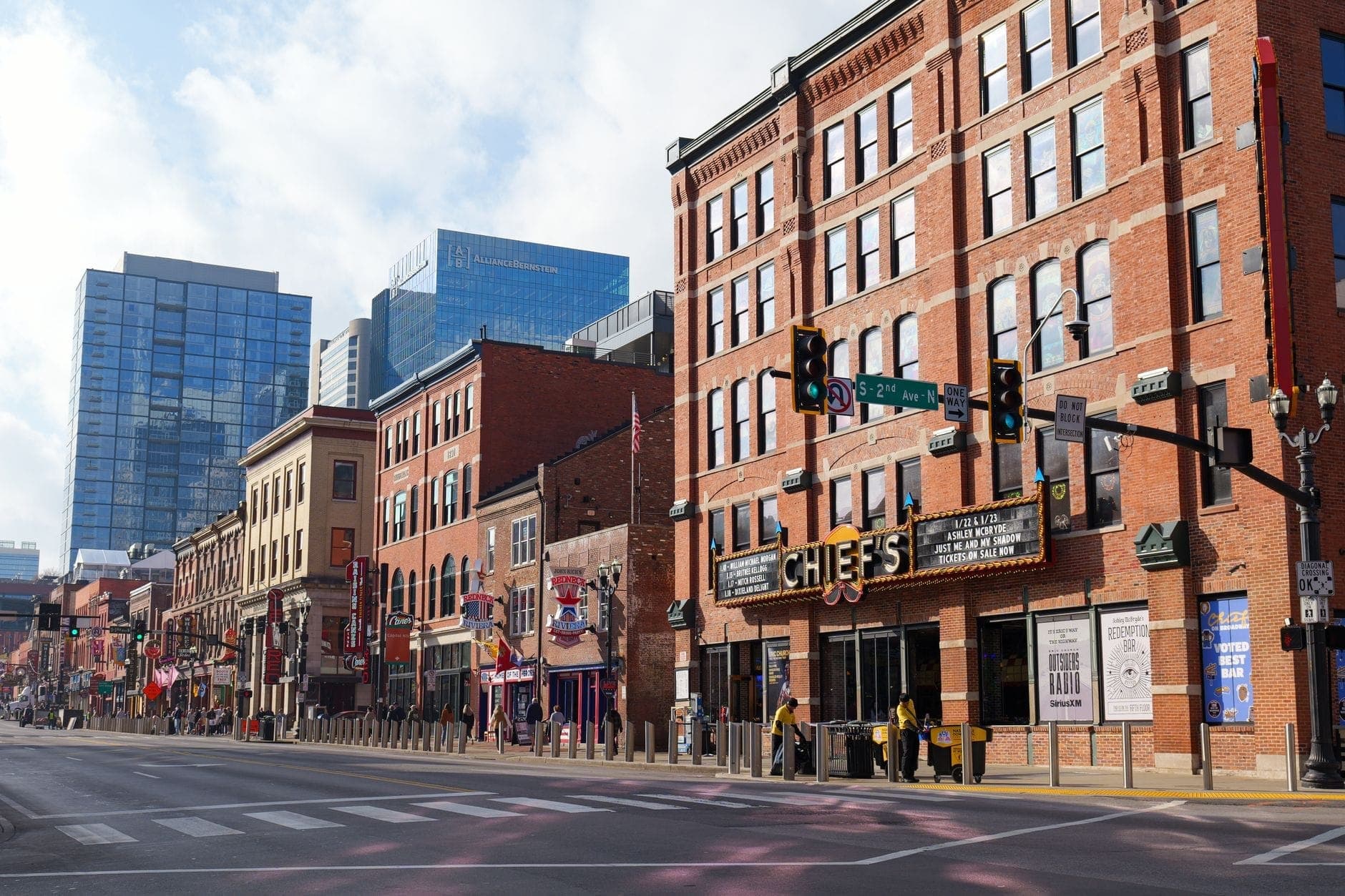 Tagesszene einer Straße in der Innenstadt von Nashville mit historischen Backsteingebäuden, Leuchtreklamen und modernen Wolkenkratzern im Hintergrund.