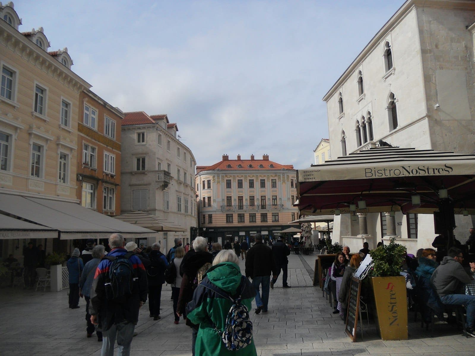 I turisti passeggiano in una piazza lastricata di pietra fiancheggiata da edifici storici e caffè nel centro di Spalato, in Croazia.
