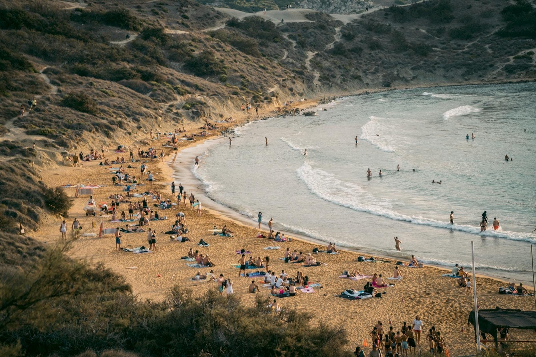 Ein breiter Sandstrand am Fuß grüner Klippen mit badenden und entspannenden Menschen, sanften Wellen und unberührter Natur an der Għajn Tuffieħa Bay.