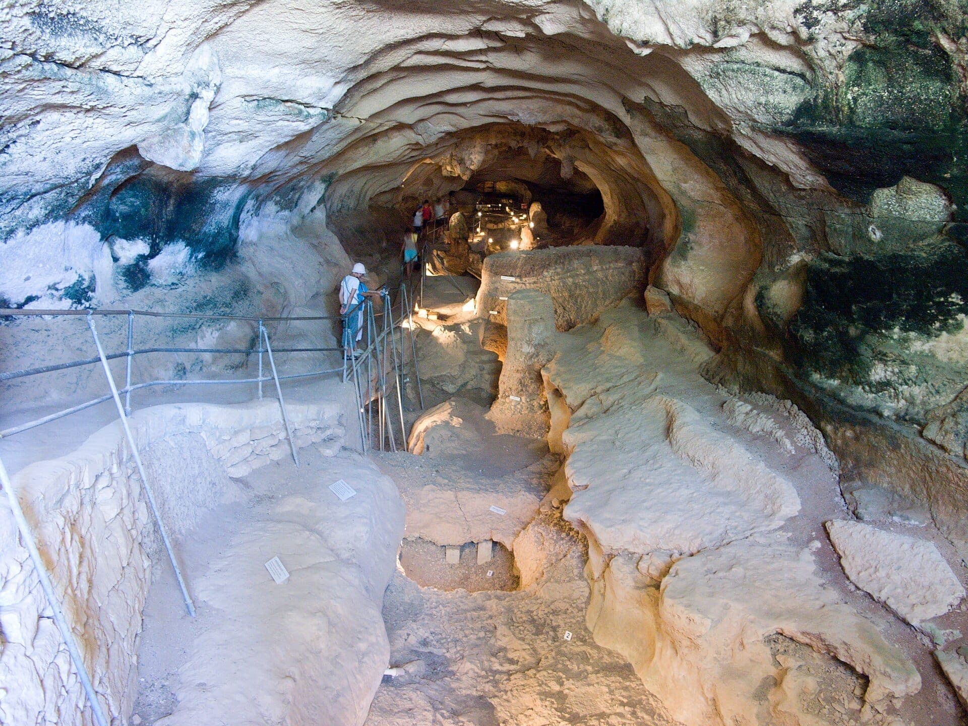 Besucher erkunden den beleuchteten Innenweg der Għar Dalam Höhle in Malta, umgeben von rauen Felsformationen und uralten geologischen Schichten.