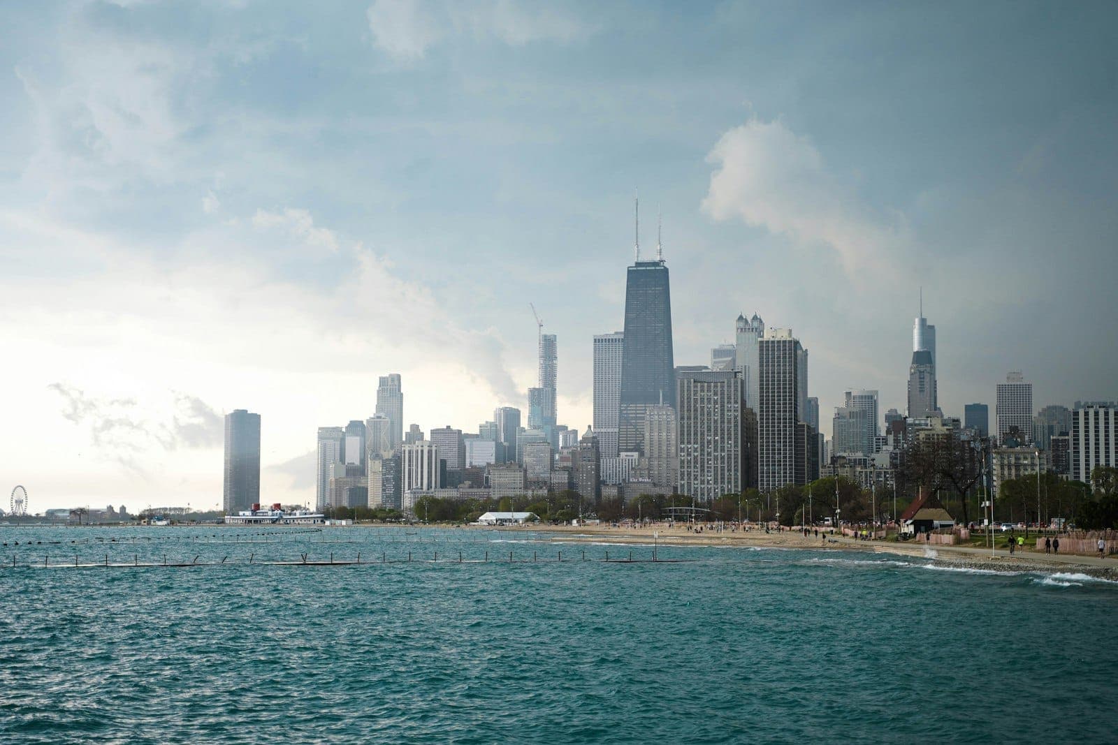 Dramatic view of Chicago’s Gold Coast from the lake, showing the city skyline, sandy beach, and vibrant water under a partly cloudy sky.