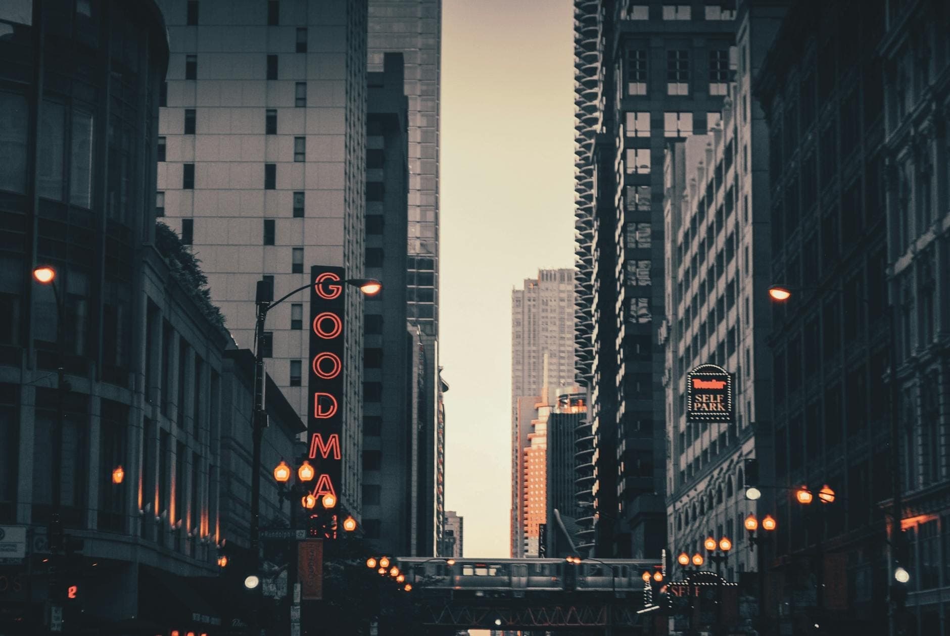 มุมมองบนถนนชิคาโก เห็นป้ายนีออนแนวตั้งของ Goodman Theatre สว่างไสว โอบล้อมด้วยตึกระฟ้าและแสงไฟยามเย็น
