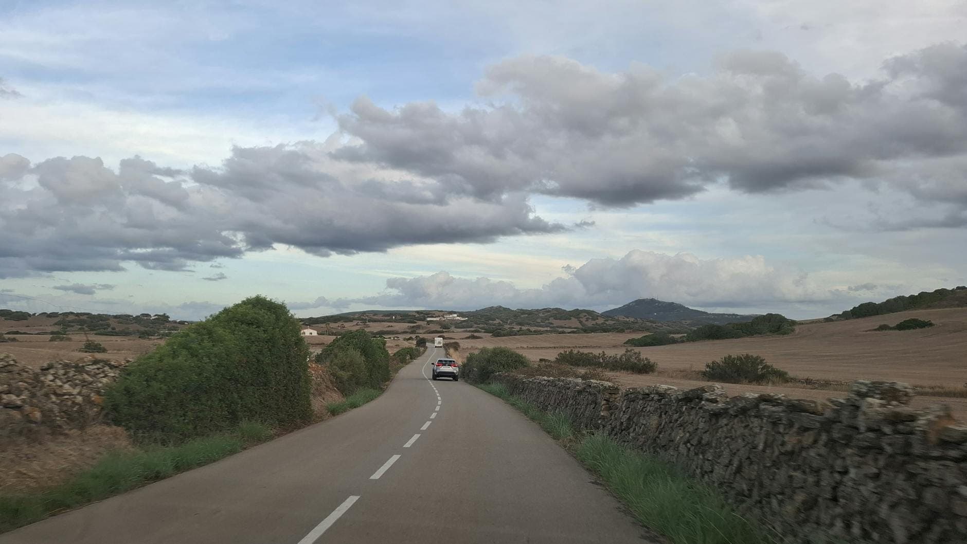 Vista de una carretera rural en Gozo, Malta, con un coche circulando entre muros de piedra y campos bajo un cielo nublado