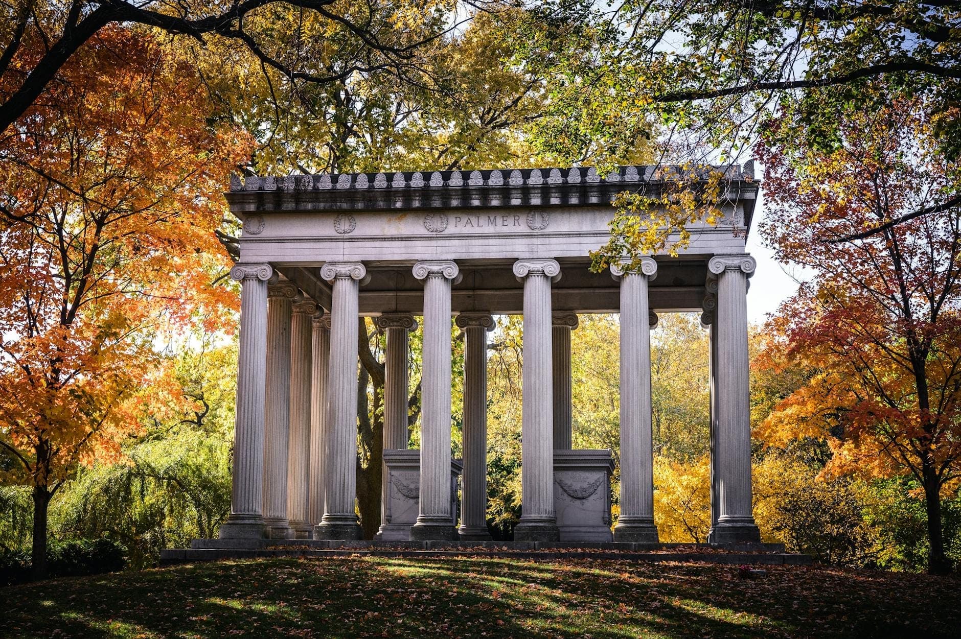 Elegant neoclassical mausoleum surrounded by colorful autumn trees in Graceland Cemetery, highlighting historic architecture and tranquil arboretum setting.