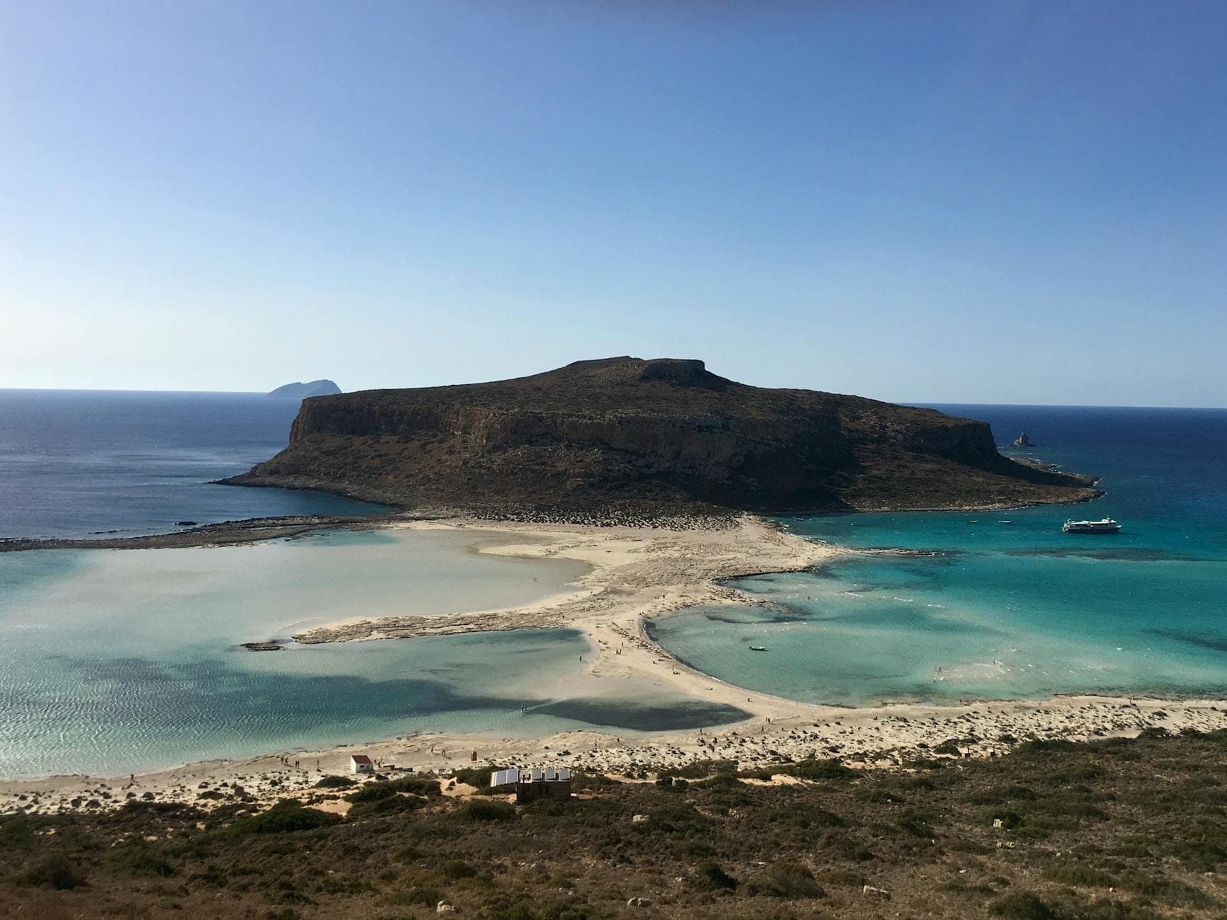 Blick auf die Insel Gramvousa mit ihren schroffen Klippen, klarem türkisfarbenem Wasser, Sandstrand und einem vor der Küste ankernden Boot unter blauem Himmel.