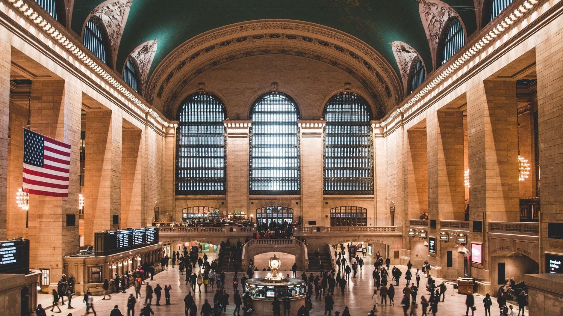 มุมกว้างของ Main Concourse ใน Grand Central Terminal เห็นหน้าต่างโค้ง ไฟอเมริกัน และผู้คนที่คึกคักใต้เพดานลายดวงดาวสีเขียว