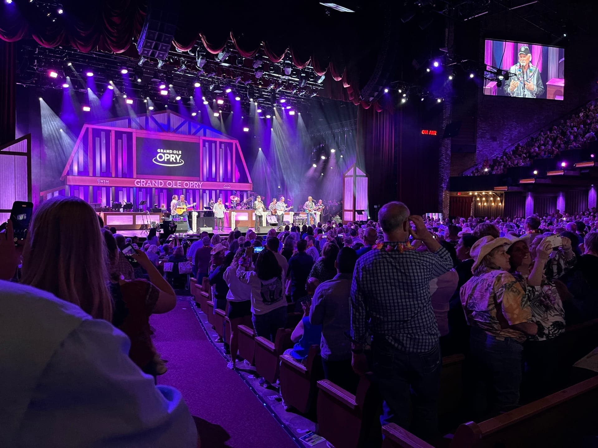 Packed audience at the Grand Ole Opry House watching a live country music performance on a brightly lit stage in Nashville.