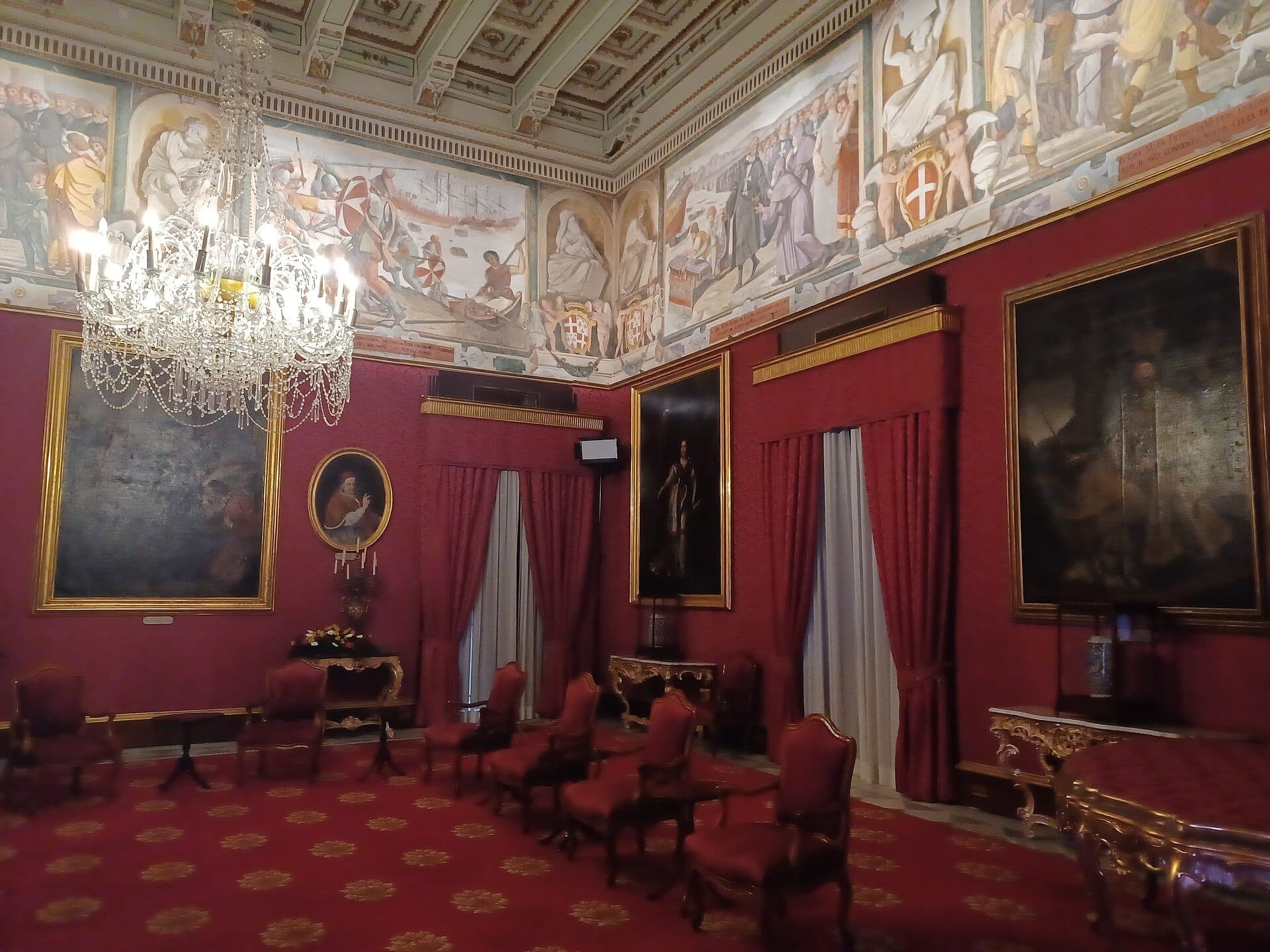 Opulenter Staatsraum im Inneren des Palastes des Großmeisters in Valletta, mit prunkvollen Kronleuchtern, roter Polsterung, goldverzierten Möbeln und historischen Gemälden an den Wänden.