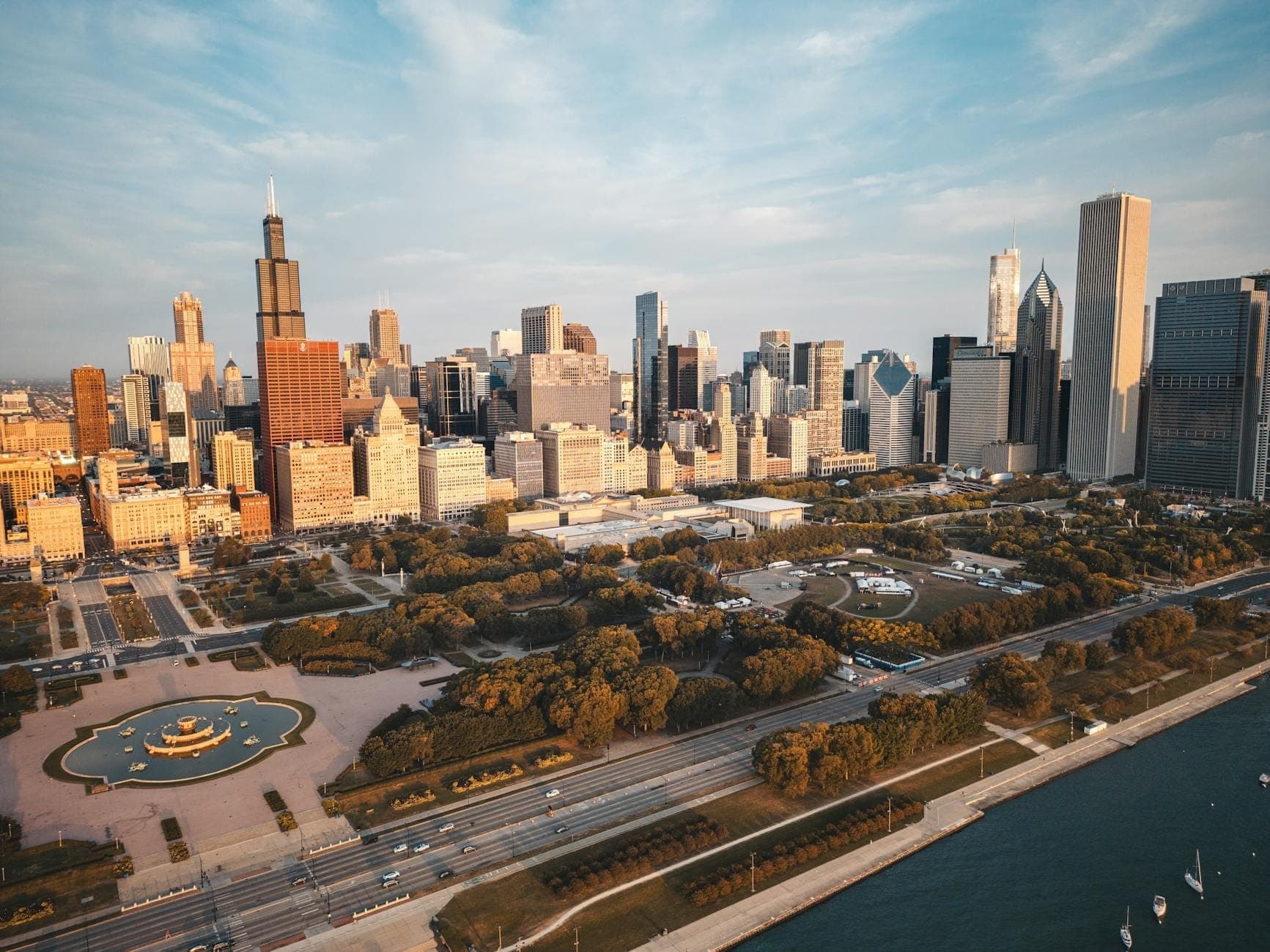 Aerial view of Grant Park with Buckingham Fountain, downtown Chicago skyline, and Lake Michigan in the golden evening light.