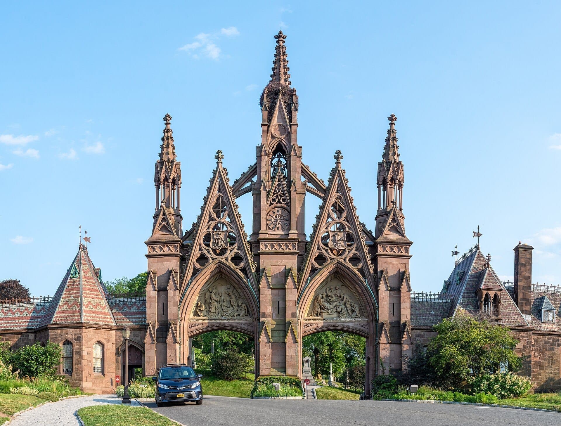 ประตูทางเข้าสไตล์ Gothic Revival ที่華丽งดงามของ Green-Wood Cemetery ในบรูคลิน ตัดกับท้องฟ้าสีฟ้าใสและรายละเอียดทางสถาปัตยกรรม