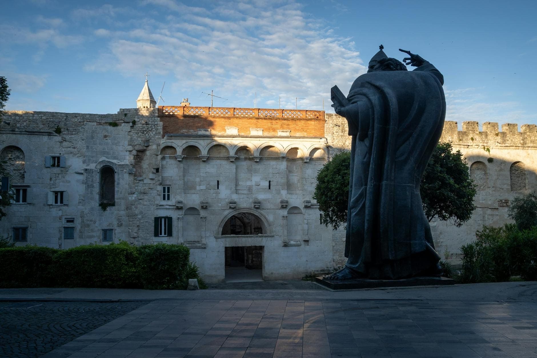 La statua di Gregorio di Nin si erge maestosa davanti alle antiche mura di pietra e agli archi del Palazzo di Diocleziano a Spalato, in Croazia.