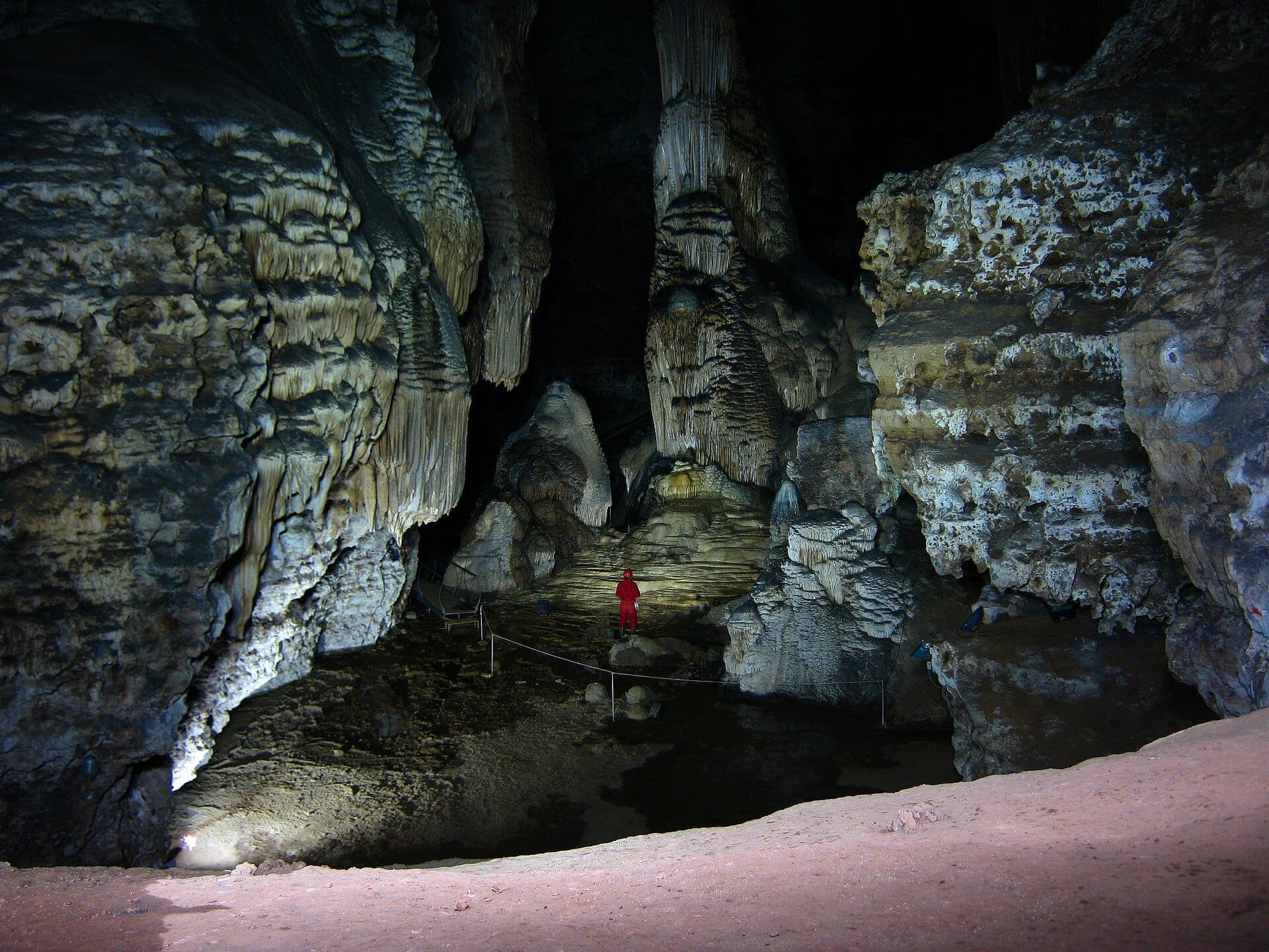 Grandes cámaras de piedra caliza, formaciones de estalactitas y un visitante con traje rojo en el interior de la cueva Grotte Su Marmuri en Ulassai, Cerdeña.