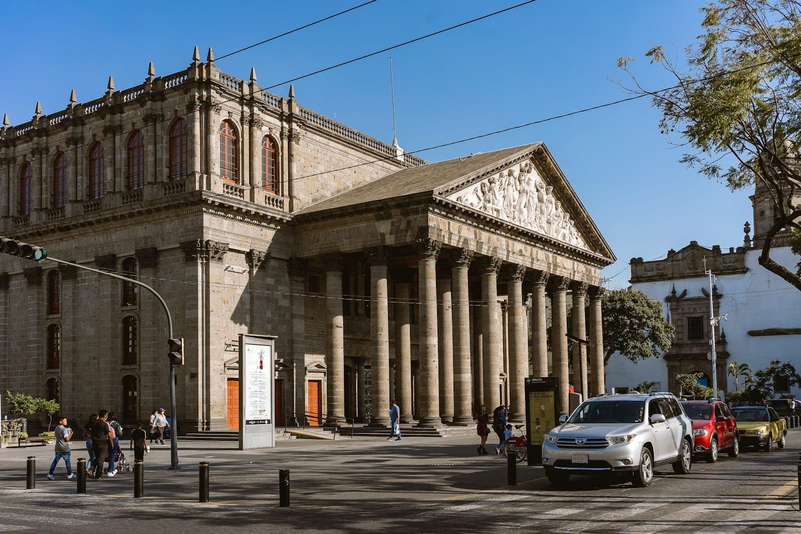 วิวกลางวันของด้านหน้าสถาปัตยกรรมนีโอคลาสสิกของ Teatro Degollado พร้อมเสาคอรินเทียน ประติมากรรมนูนต่ำ และผู้คนด้านหน้าในกวาดาลาฮารา