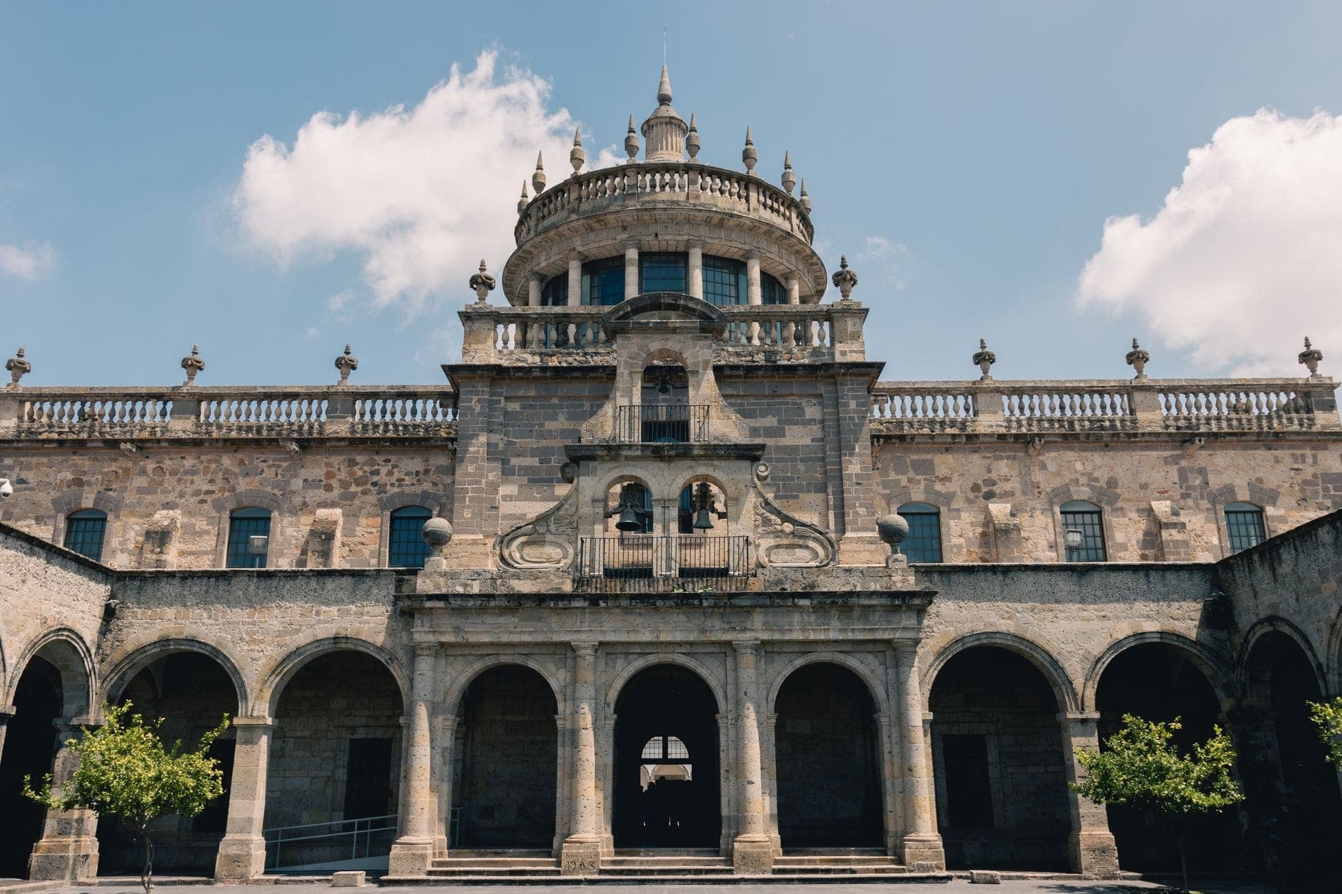 มุมมองด้านหน้าของ Hospicio Cabañas ในกัวดาลาฮารา แสดงให้เห็นสถาปัตยกรรมอันยิ่งใหญ่และโดมกลางใต้ท้องฟ้าสีฟ้าที่มีเมฆ