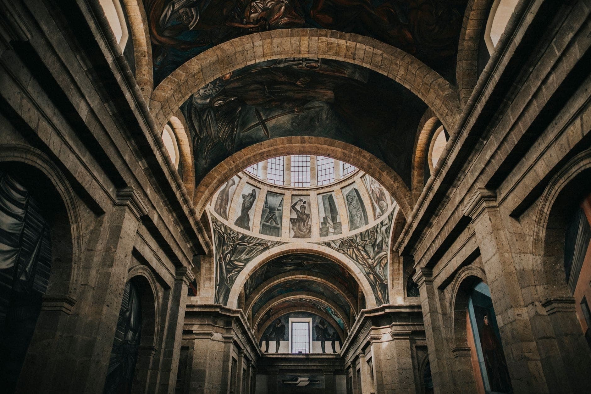 วิวกว้างของภายใน Hospicio Cabañas พร้อมโถงหินโค้งและจิตรกรรมฝาผนังชื่อดังของ Orozco ใต้เพดานโดม