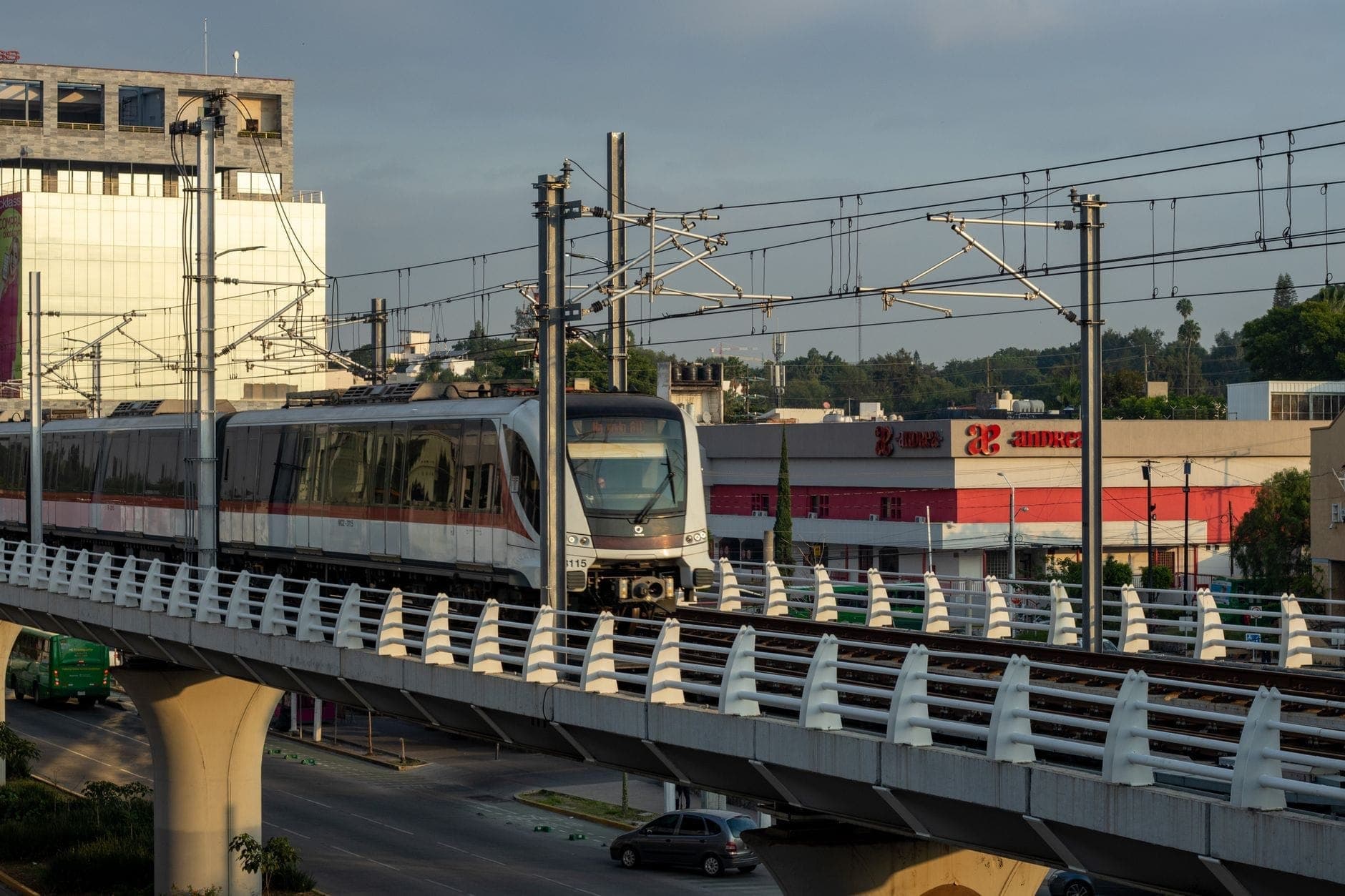 รถไฟฟ้าใต้ดินยกระดับวิ่งบนสะพานเหนือถนนในเมือง Guadalajara โดยมีสายไฟฟ้าเหนือศีรษะและอาคารเป็นฉากหลัง
