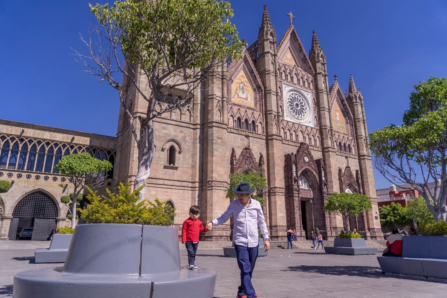 เด็กๆ เล่นอยู่บนลานกว้างที่แดดสดใสด้านหน้า Templo Expiatorio โบสถ์กอธิคที่มีชื่อเสียงในกวาดาลาฮารา พร้อมครอบครัวที่สนุกสนานกับบรรยากาศกลางแจ้ง