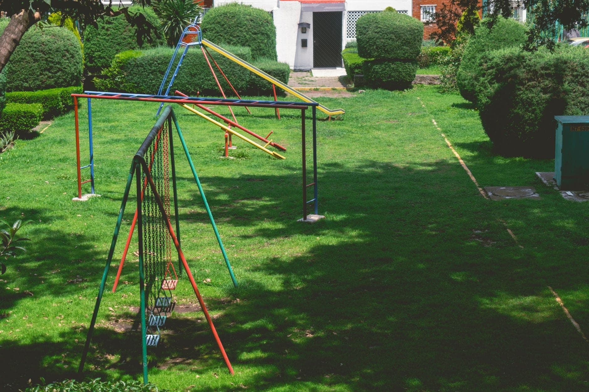 สวนสาธารณะในย่านที่พักอาศัยสีเขียวขจีในเมือง Guadalajara พร้อมอุปกรณ์สนามเด็กเล่นหลากสี ลานสไลเดอร์ และพุ่มไม้ตัดแต่งใต้ท้องฟ้าแดดจ้า