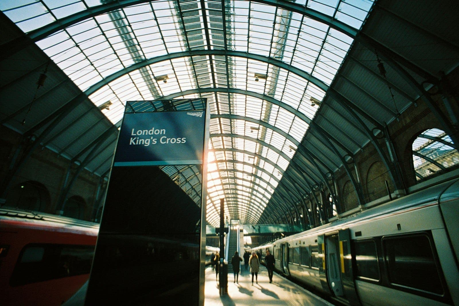 Innenraum des Bahnhofs London King's Cross mit gewölbtem Glasdach, Zügen auf den Bahnsteigen und einem Schild mit der Aufschrift 'London King's Cross'.