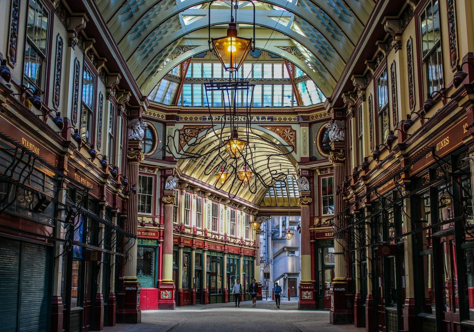 Blick auf den verzierten überdachten Gang des Leadenhall Market mit grün-dunkelrotem Dach, Vintage-Laternen und dekorativen Ladengeschäften in London.