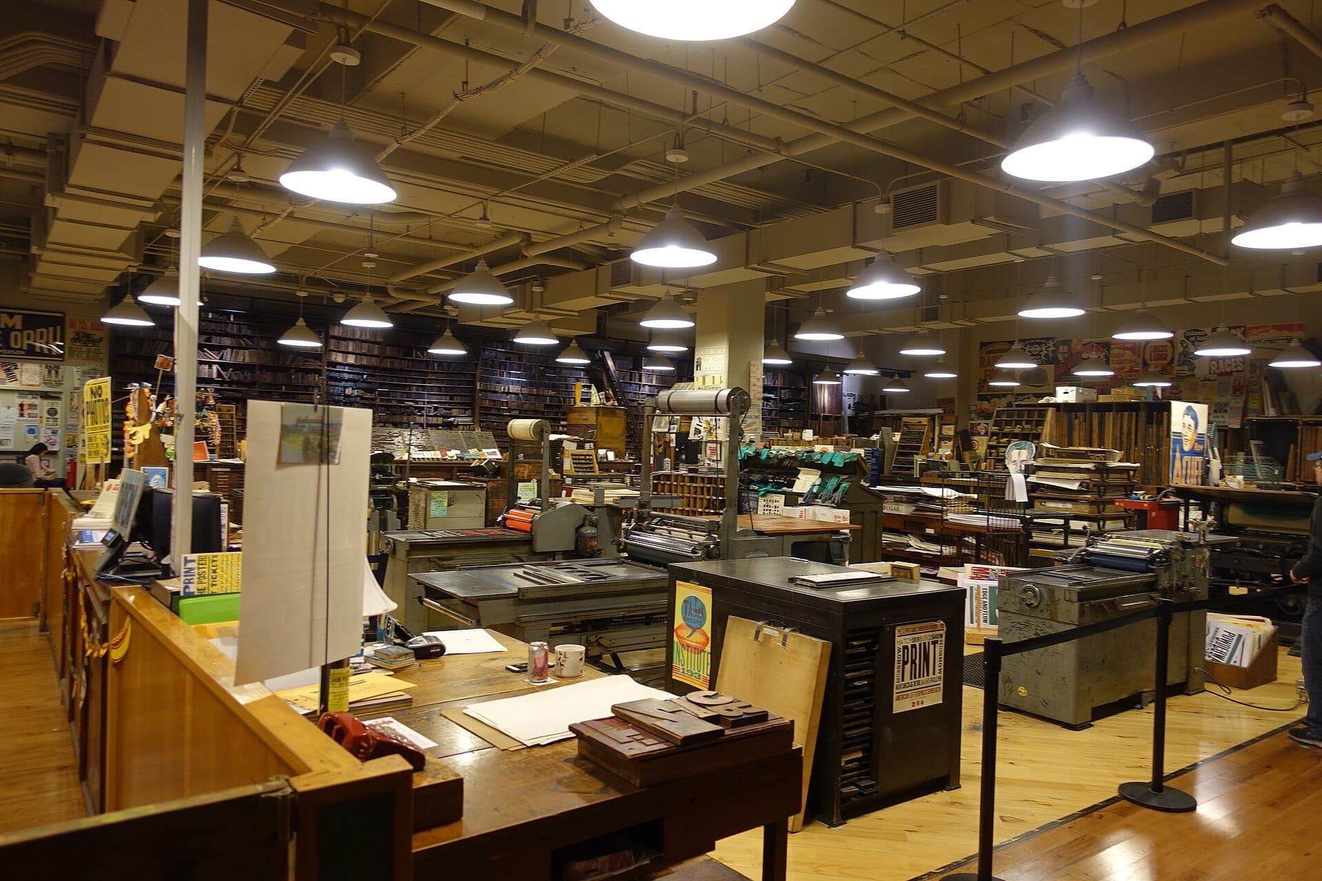 Innenansicht von Hatch Show Print in Nashville, mit Vintage-Hochdruckmaschinen, Holzböden und beleuchteten Industriedeckenleuchten.
