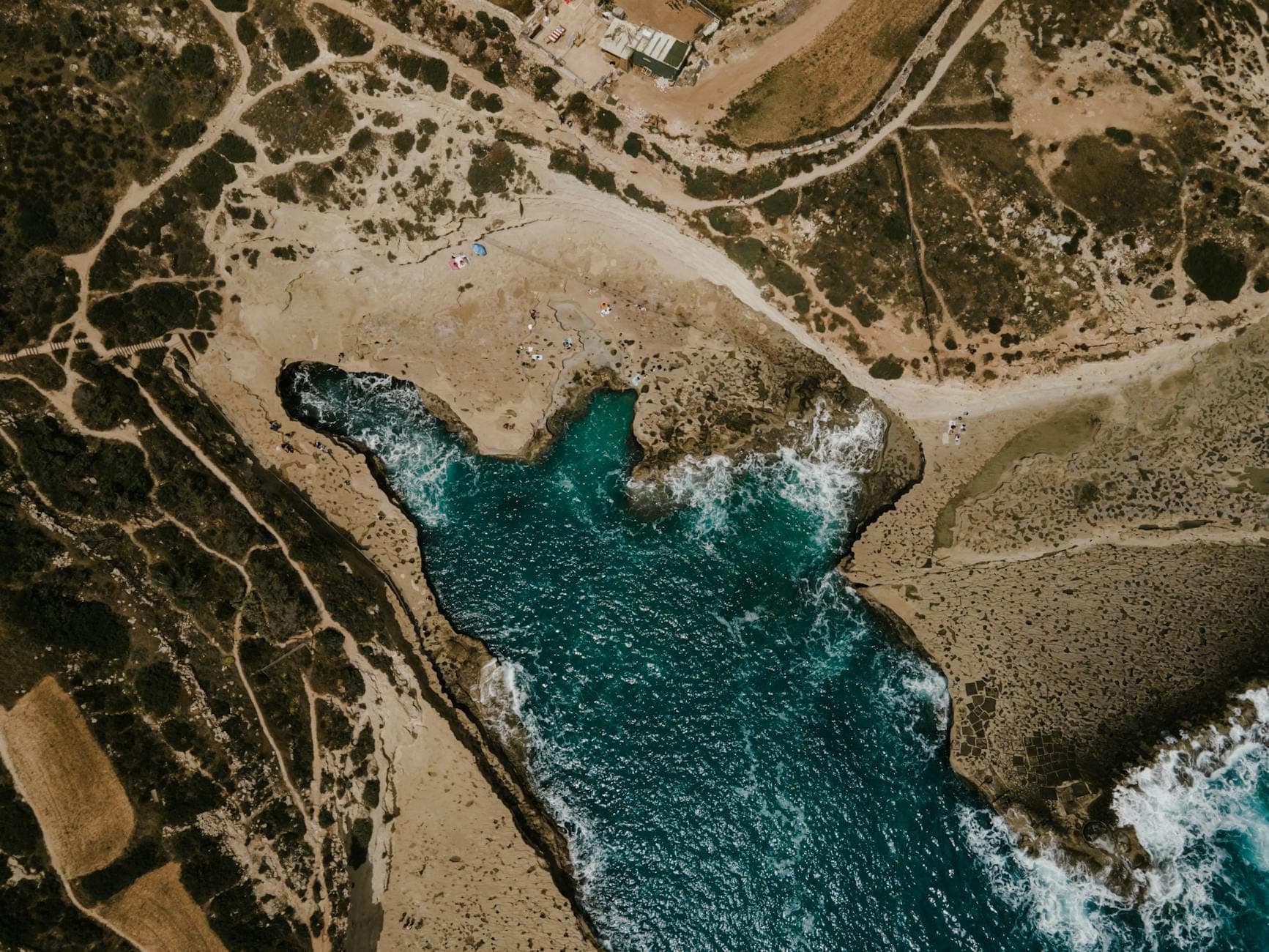 Luftaufnahme einer abgelegenen Felsenbucht mit klarem türkisfarbenem Wasser und einigen Menschen an einer abgelegenen Küste von Malta.