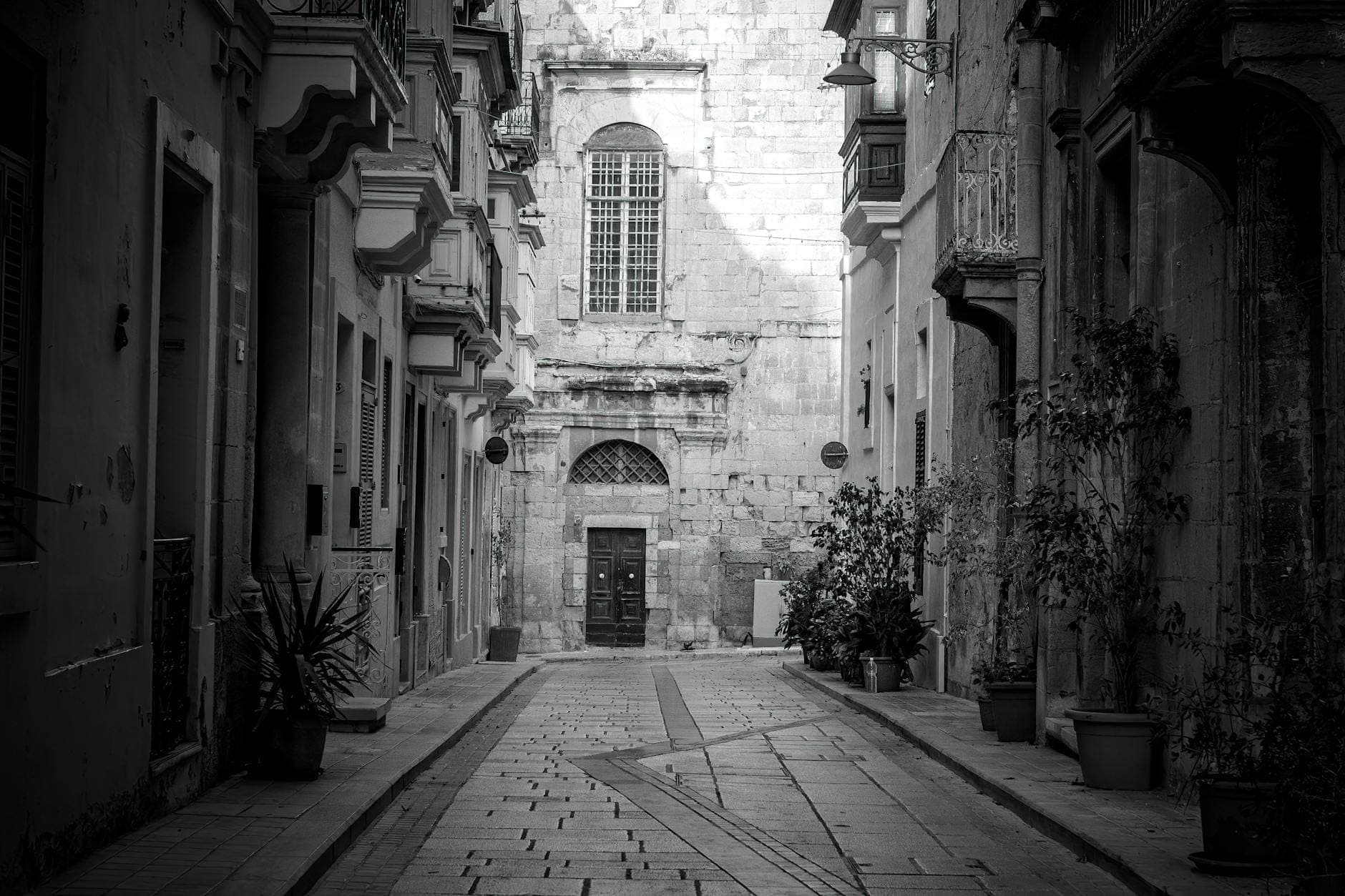 Schwarz-Weiß-Foto einer engen maltesischen Gasse mit historischen Fassaden, gewölbtem Eingang und hohen Fenstern, das eine versteckte Architektur vermittelt.