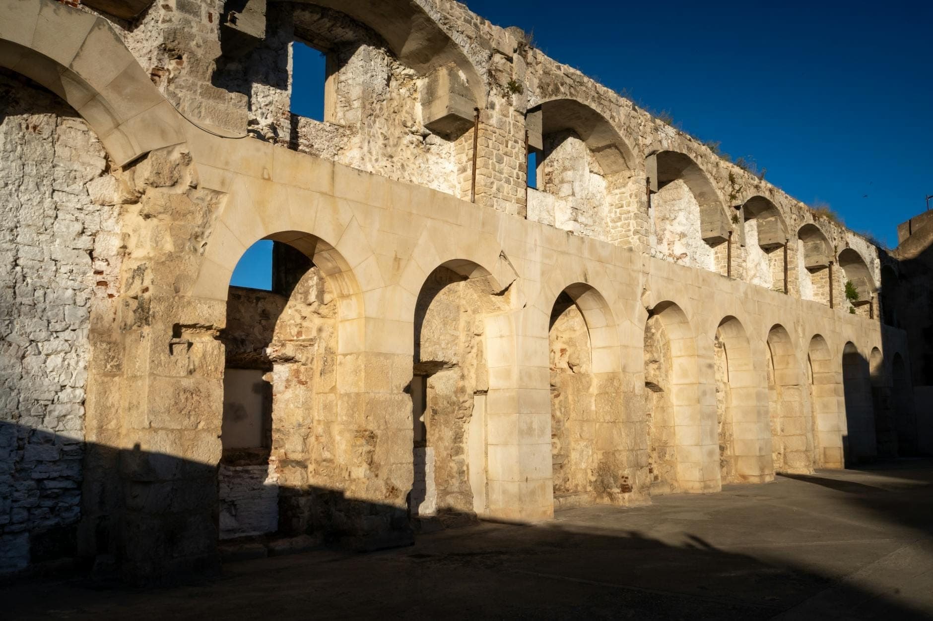Mura in pietra romane parzialmente conservate con archi in forte luce solare, che mostrano antiche rovine fuori dal Palazzo di Diocleziano a Spalato, Croazia.