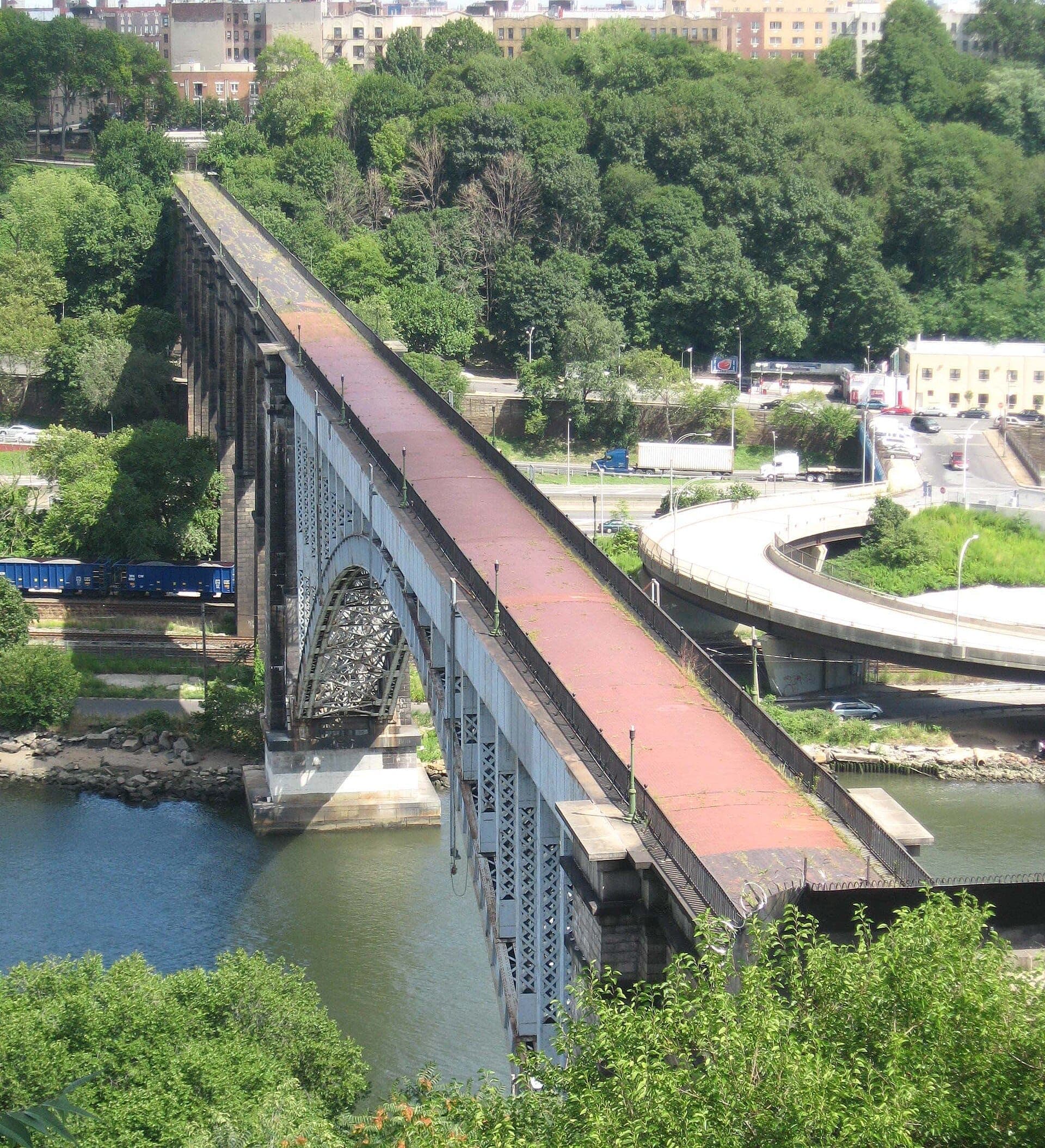 สะพาน High Bridge ทอดข้าม Harlem River ล้อมรอบด้วยต้นไม้เขียวขจีและอาคารในเมืองท่ามกลางแสงแดดสดใสใน New York City
