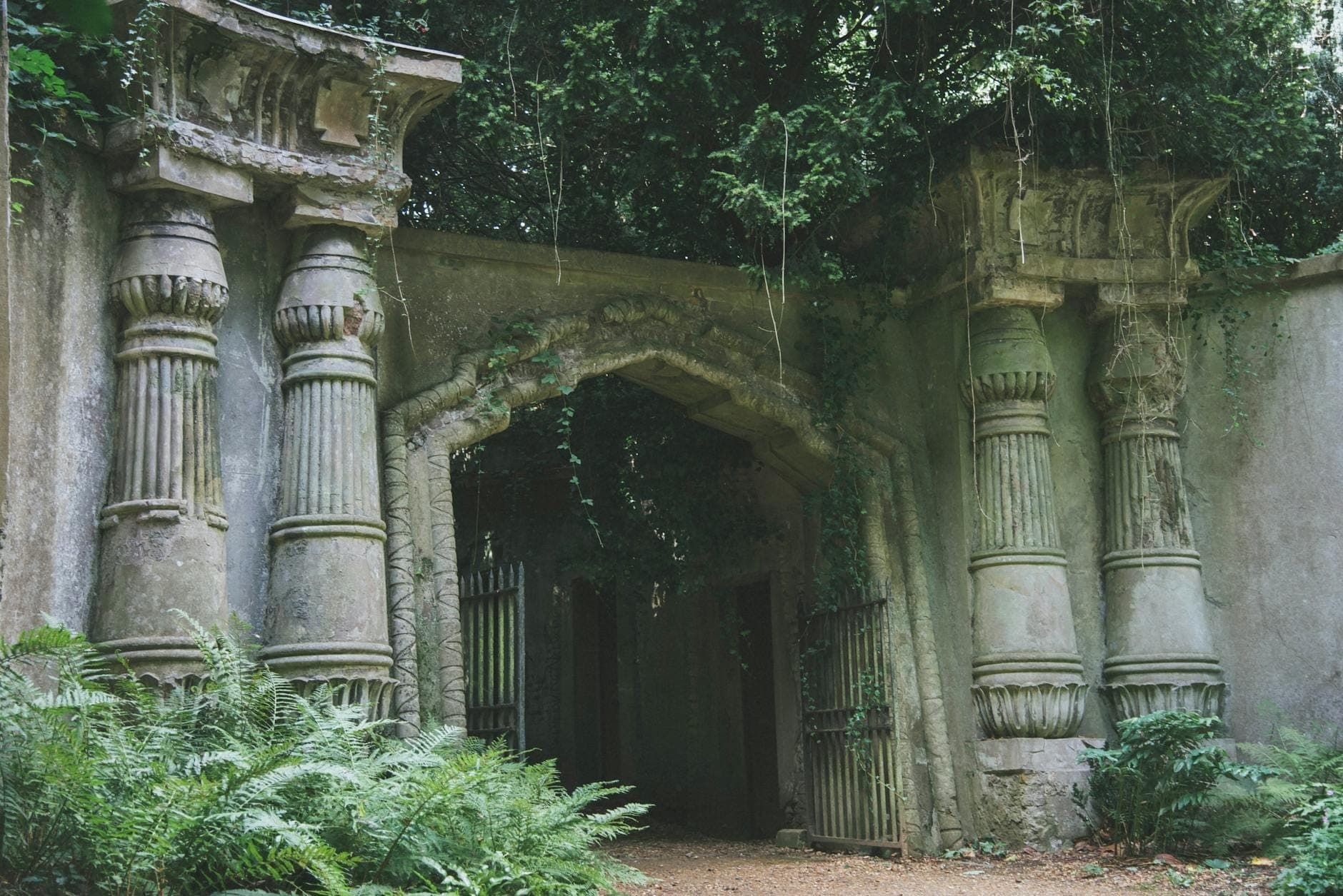 Ancienne arche victorienne couverte de mousse, flanquée de piliers imposants et encadrée d'une végétation luxuriante à l'entrée du cimetière de Highgate.