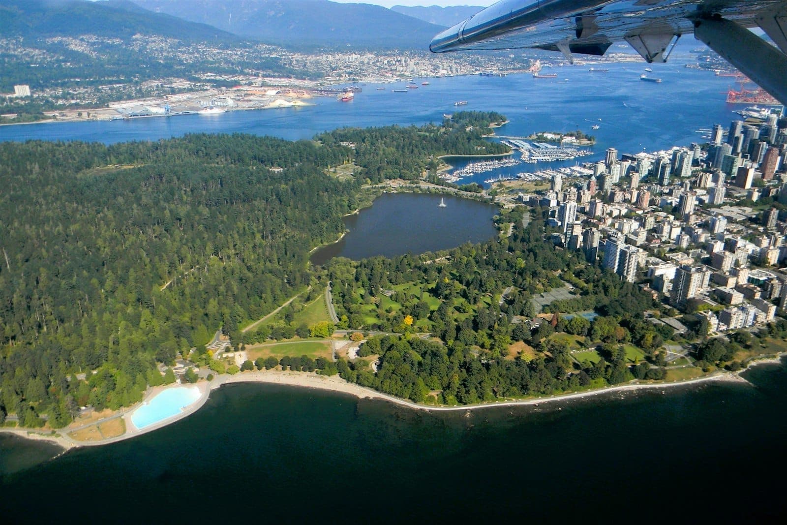 ภาพทางอากาศของป่าทึบใน Stanley Park ทะเลสาบ เส้นขอบฟ้าของเมือง และริมน้ำของ Vancouver ในวันที่อากาศแจ่มใส