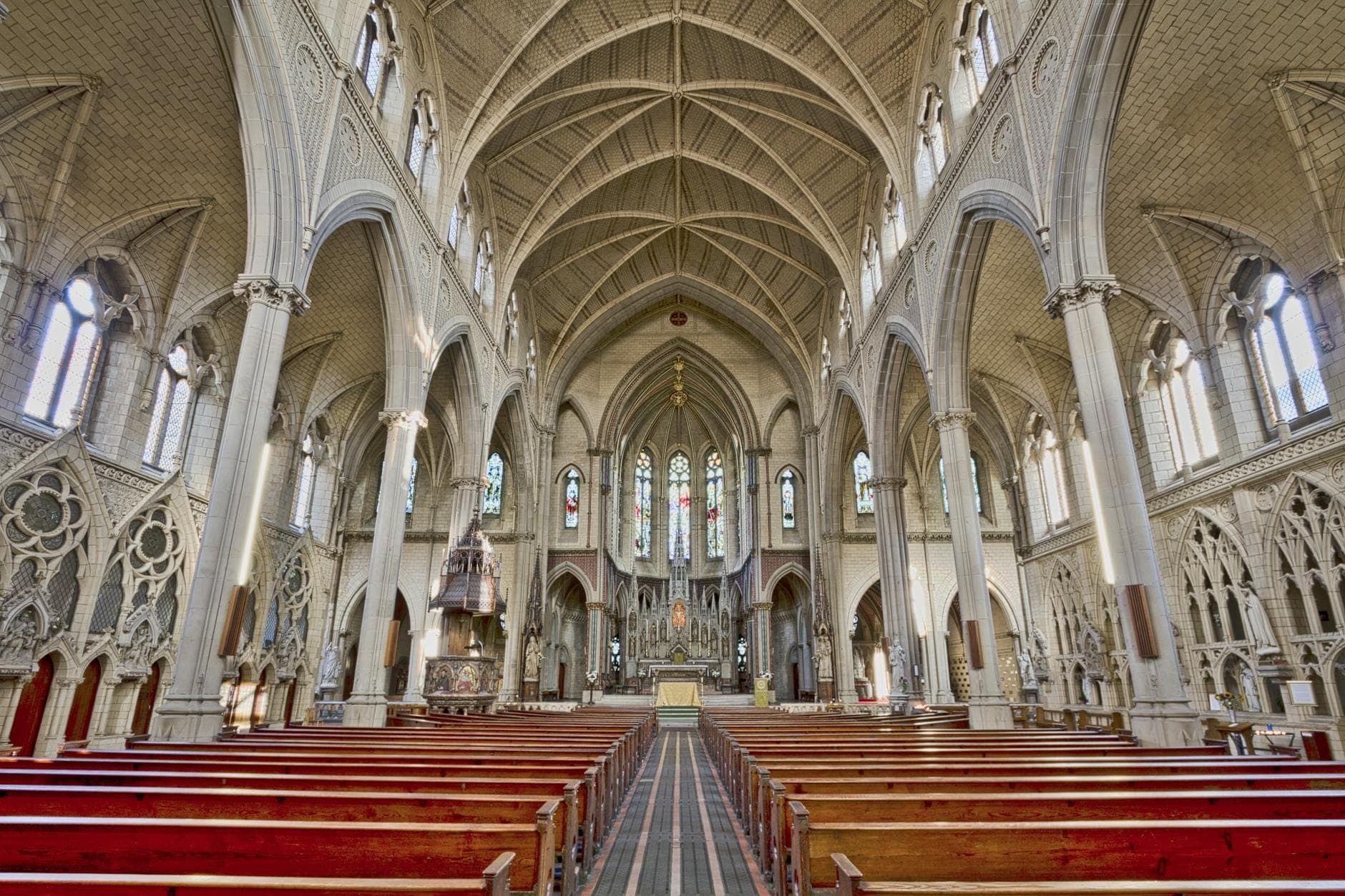 Wide-angle view of Holy Name Cathedral’s grand Gothic nave with soaring arches, stained glass windows, and red wooden pews leading toward the ornate altar.